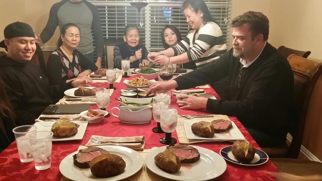 People sit around a table sharing a meal with roasted meat, side dishes, and drinks.