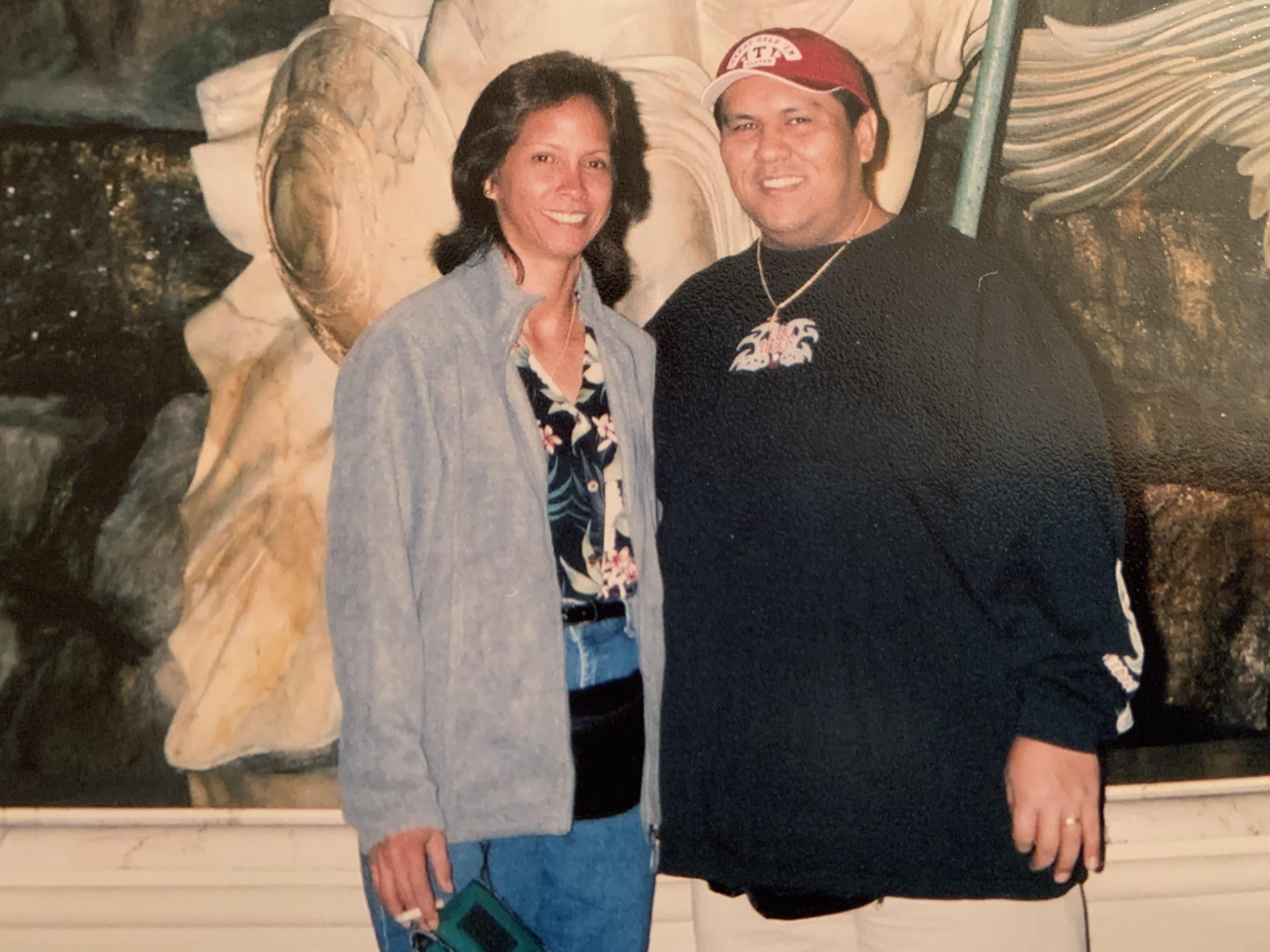 Two people pose for a picture while visiting a museum with a large statue in the background.