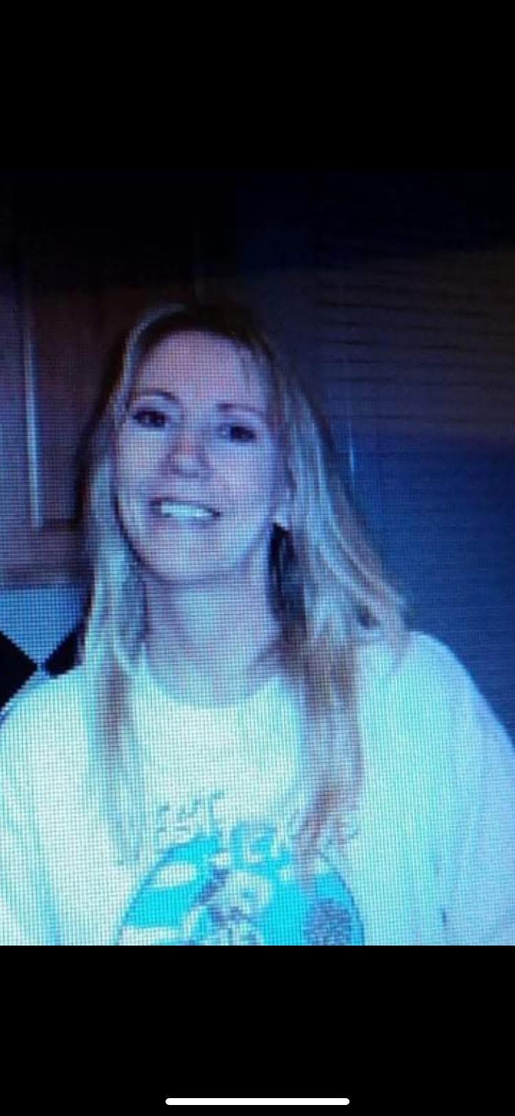 A woman smiles in a kitchen while people gather in the background during a casual afternoon event.