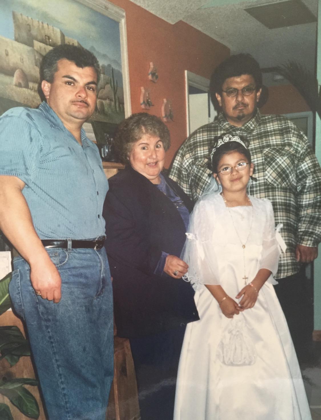 A family stands together inside a house, celebrating a young girl's special event.