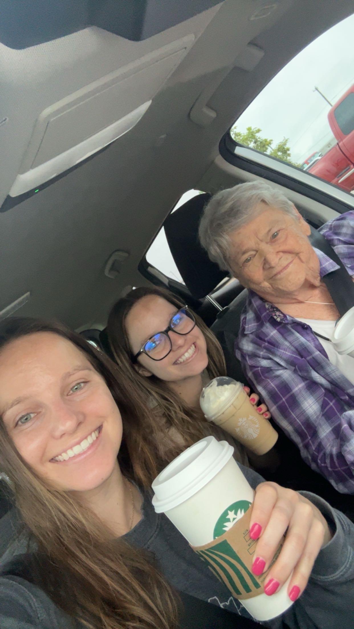 Three people sit in a car, smiling and enjoying their coffee drinks together.