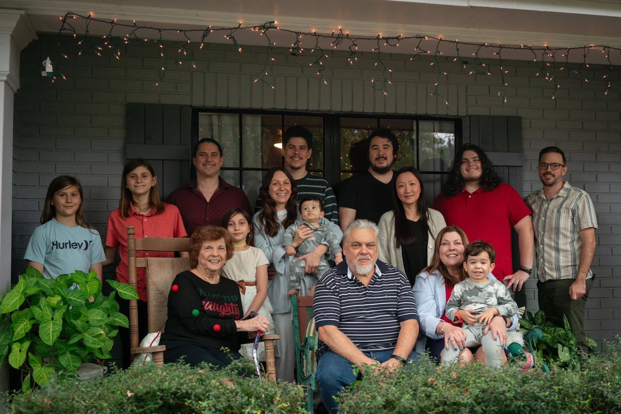 Family gathers and smiles together on the porch in the backyard during a sunny day.