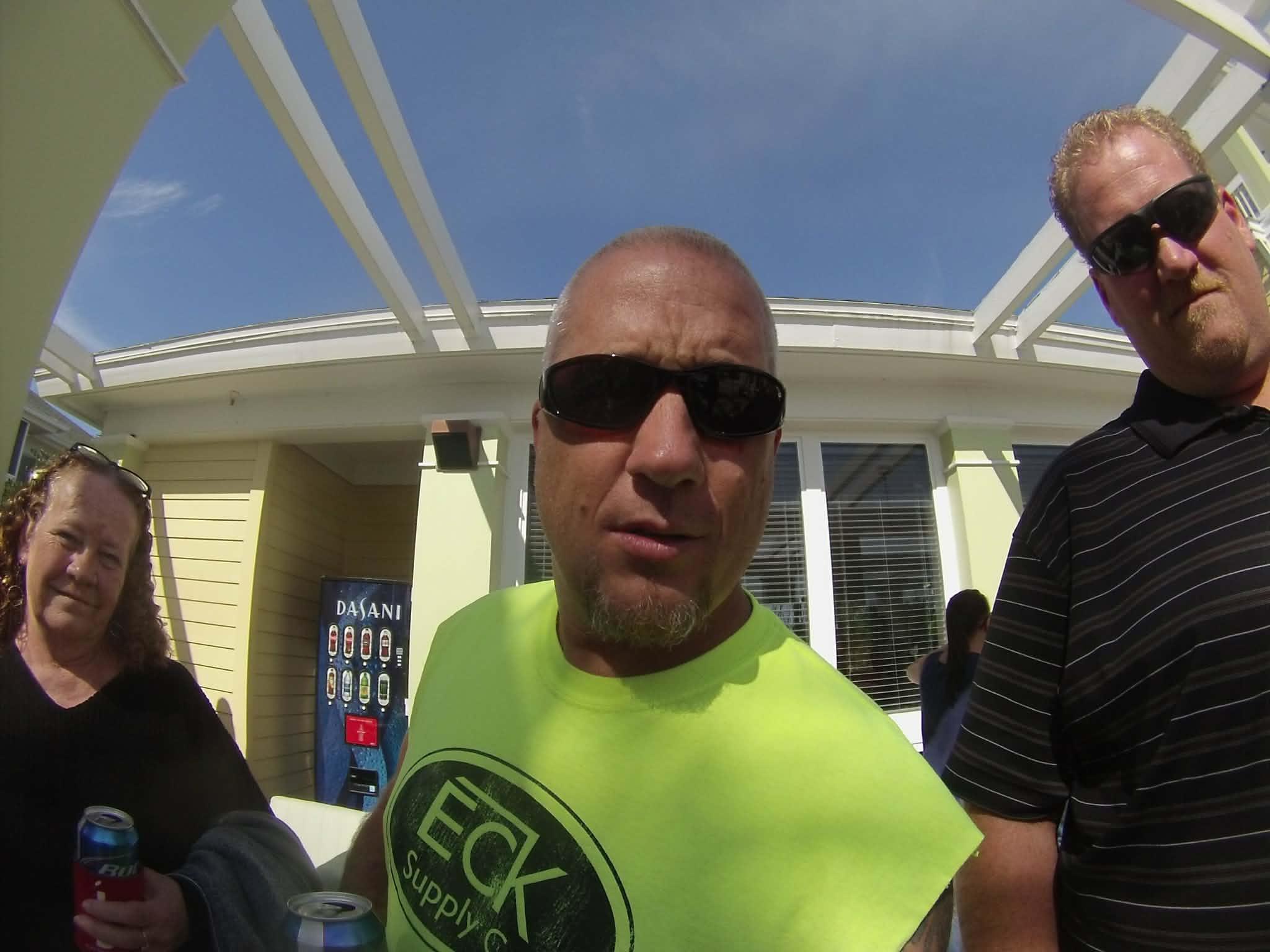 Three men interact outside a building while enjoying a sunny day with clear skies.