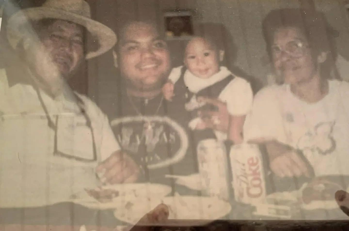 Family members enjoy food and drinks while a toddler is held by one adult. It is a casual gathering.