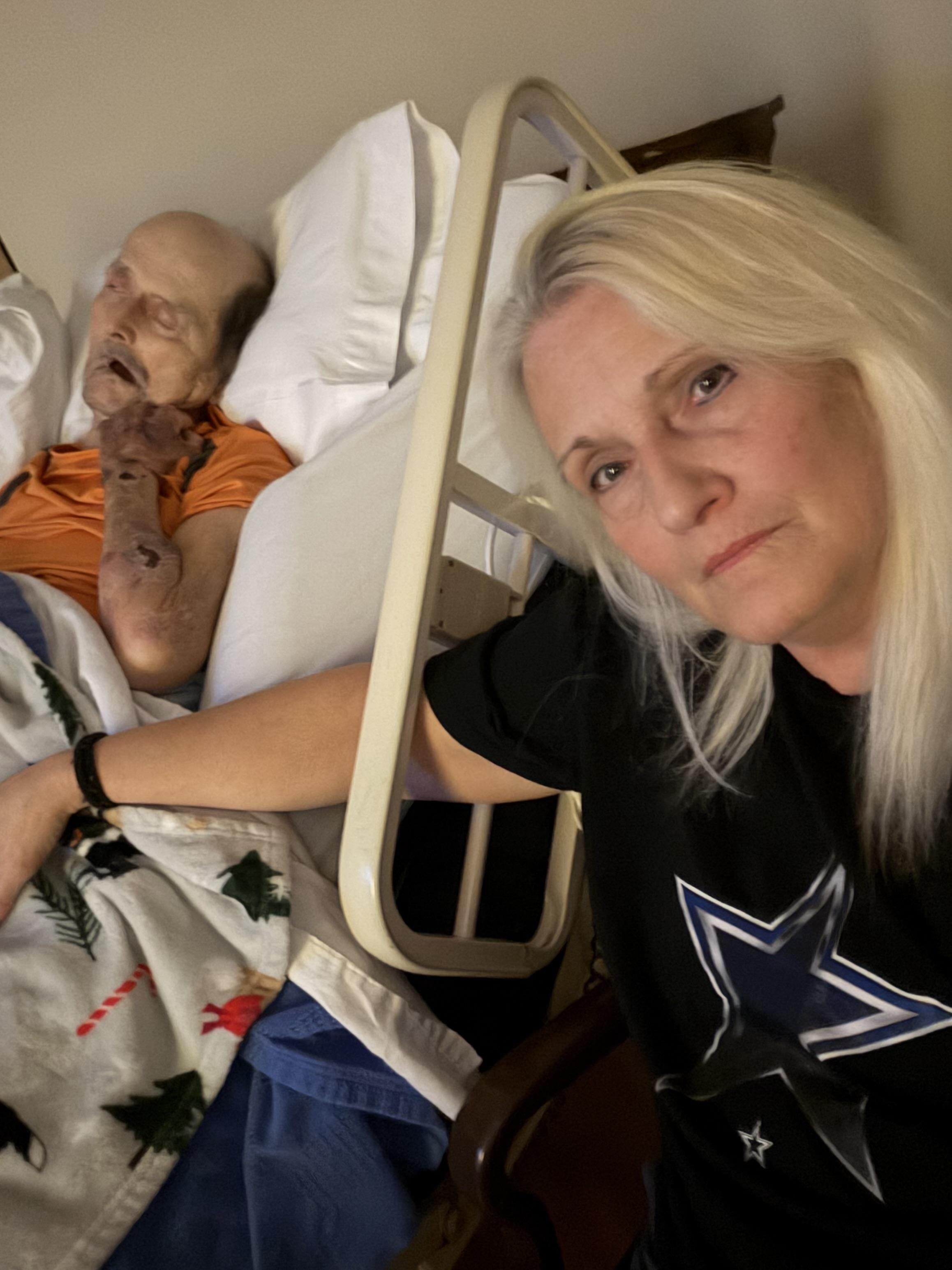A woman in a hospital bed with a man sleeping