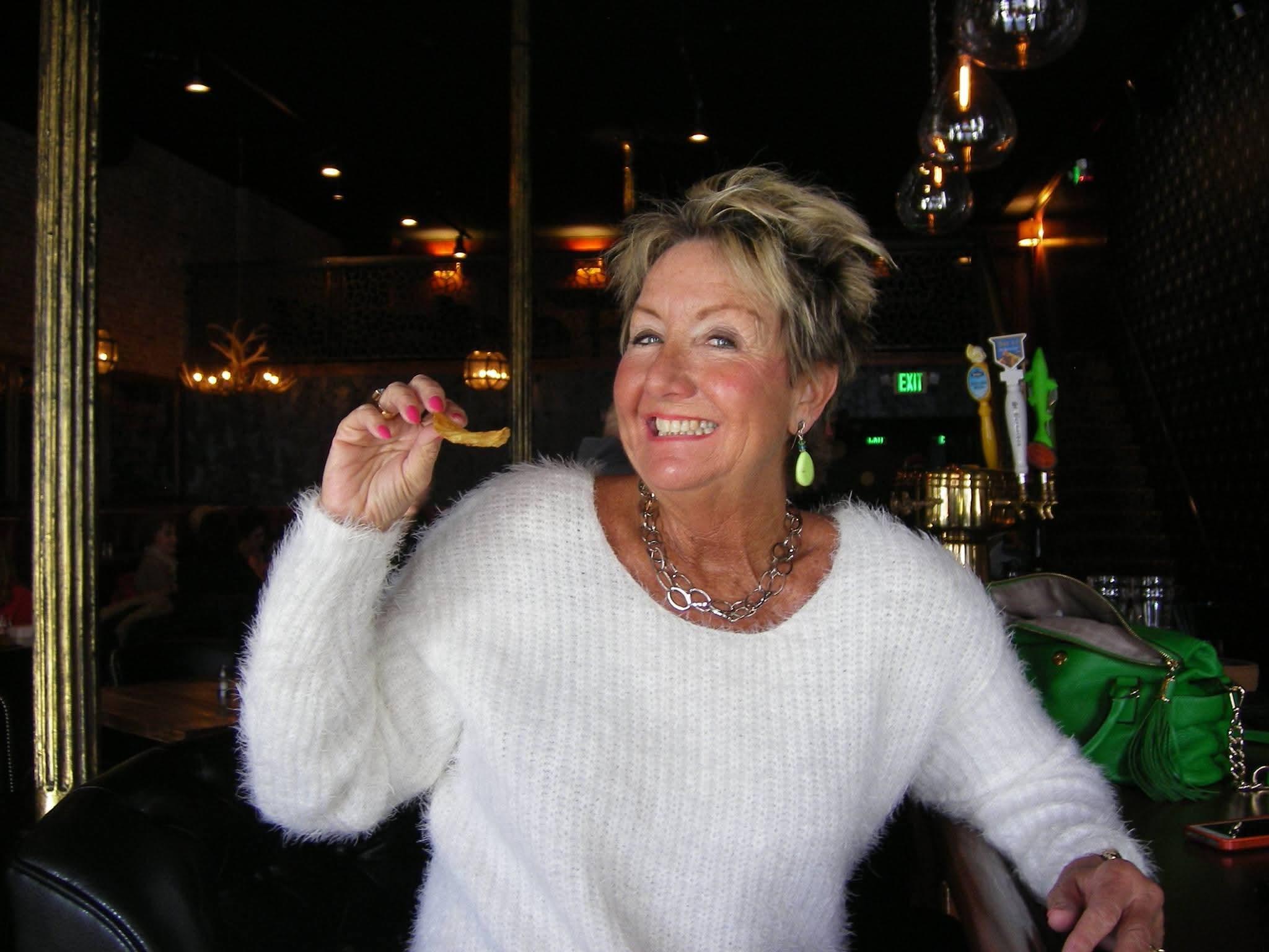 A woman enjoys a snack and smiles while spending time at a restaurant with friends.