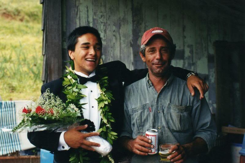 Two men at a wedding: one in a tux holding flowers, the other sipping a drink.