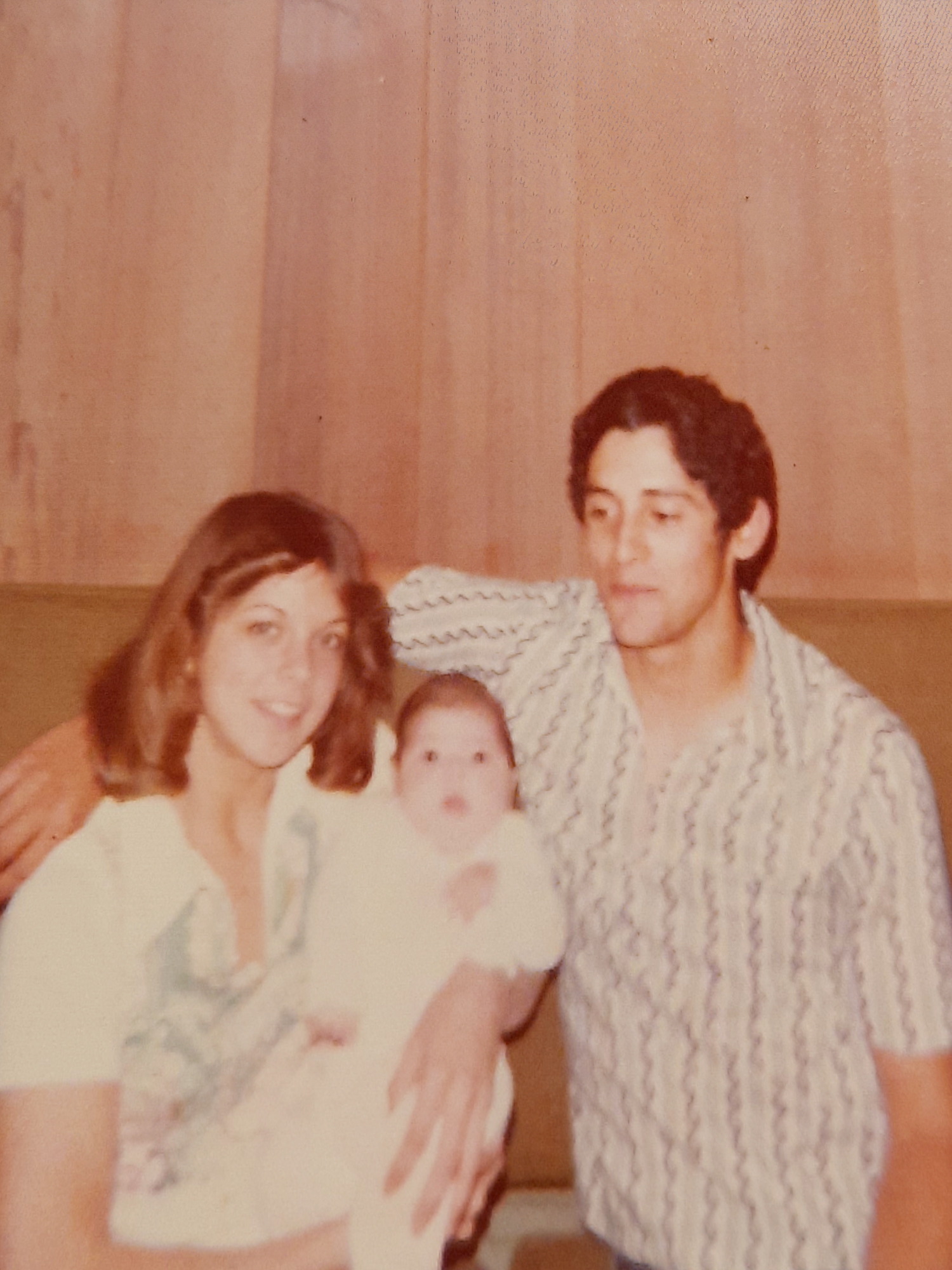 Young parents smile while holding their baby in a cozy living room setting.