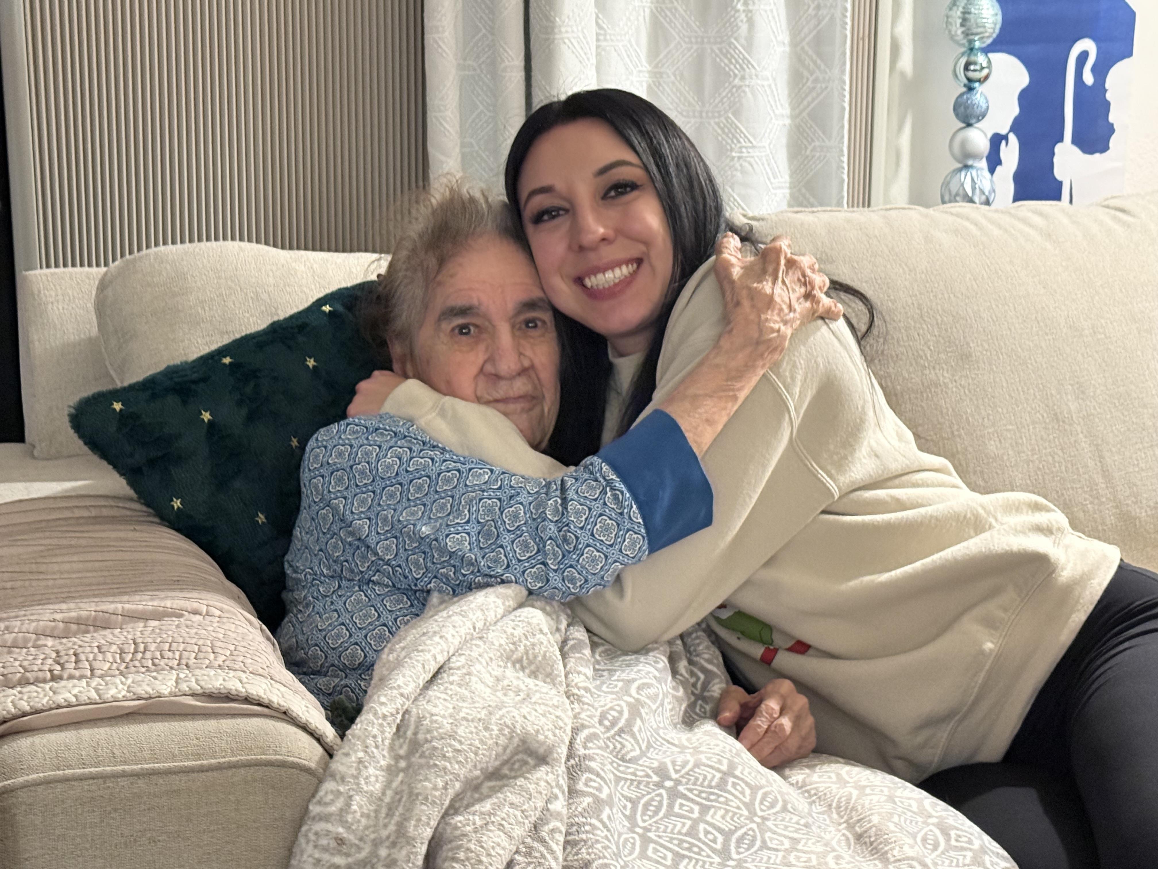A woman hugging an elderly woman on a couch