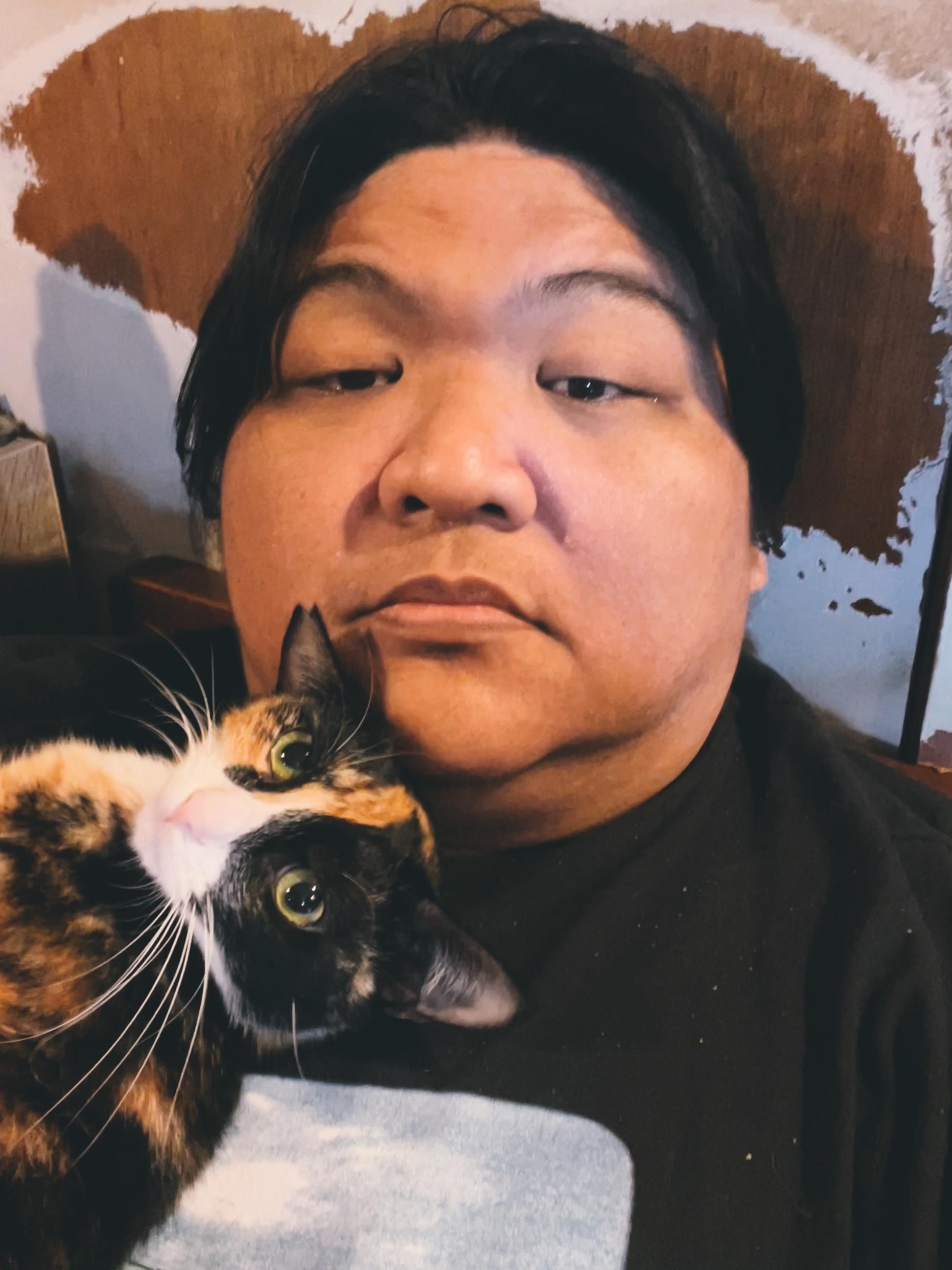 A man relaxes while holding a cat on his shoulder in a warm setting at midday.