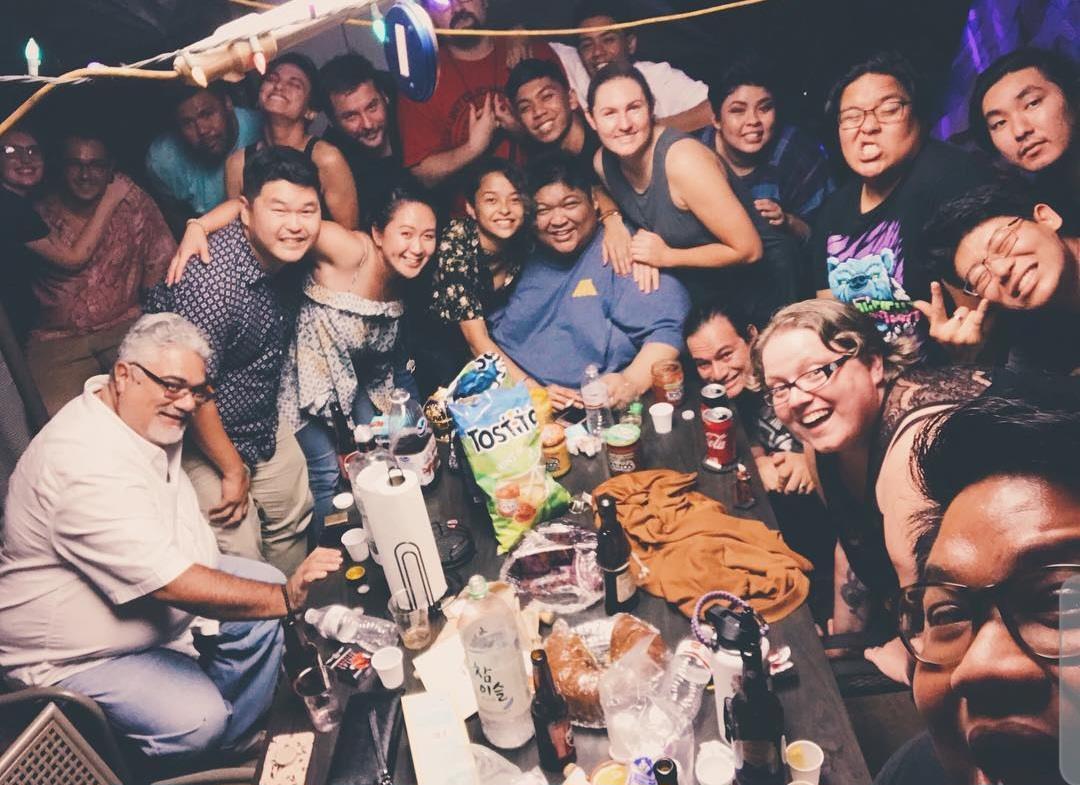 People gather around a table filled with drinks and snacks while having fun together at night.