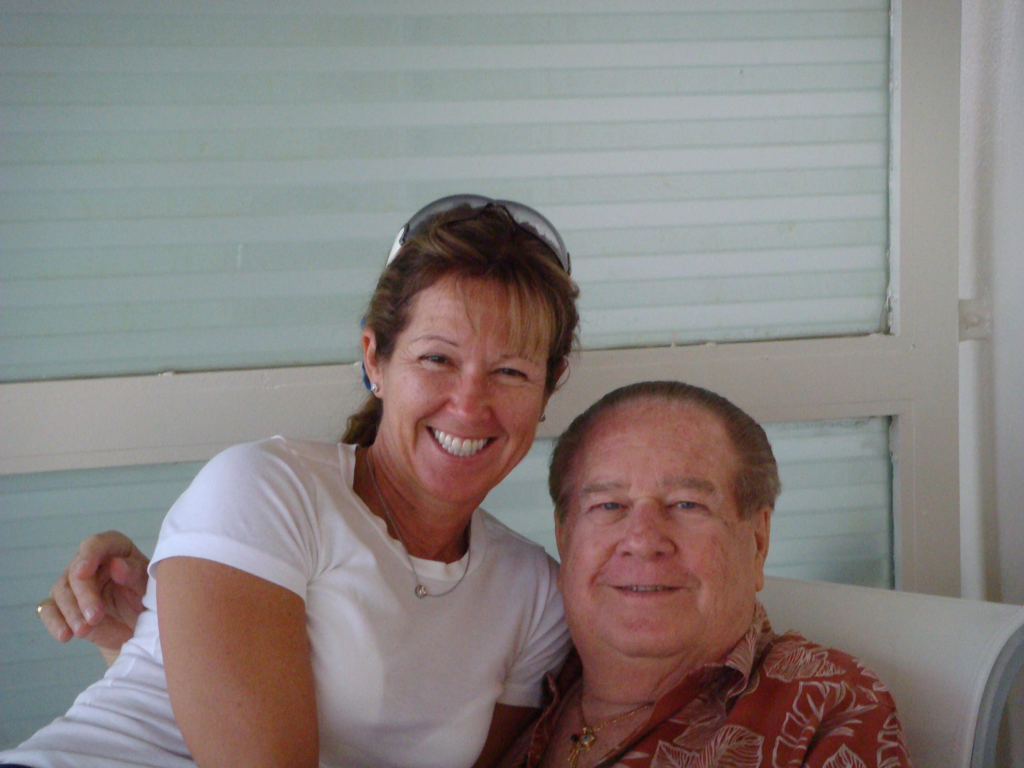 Two people smile and pose together, showing friendship and happiness while sitting indoors.