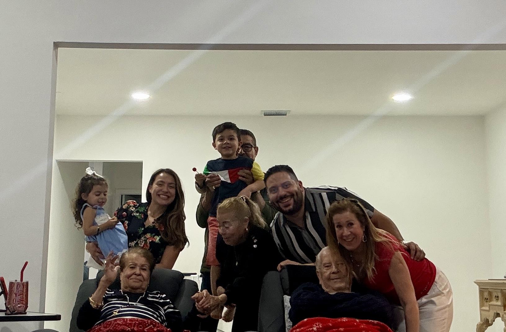 People smile and pose together in a living room. Children sit on laps of older adults.