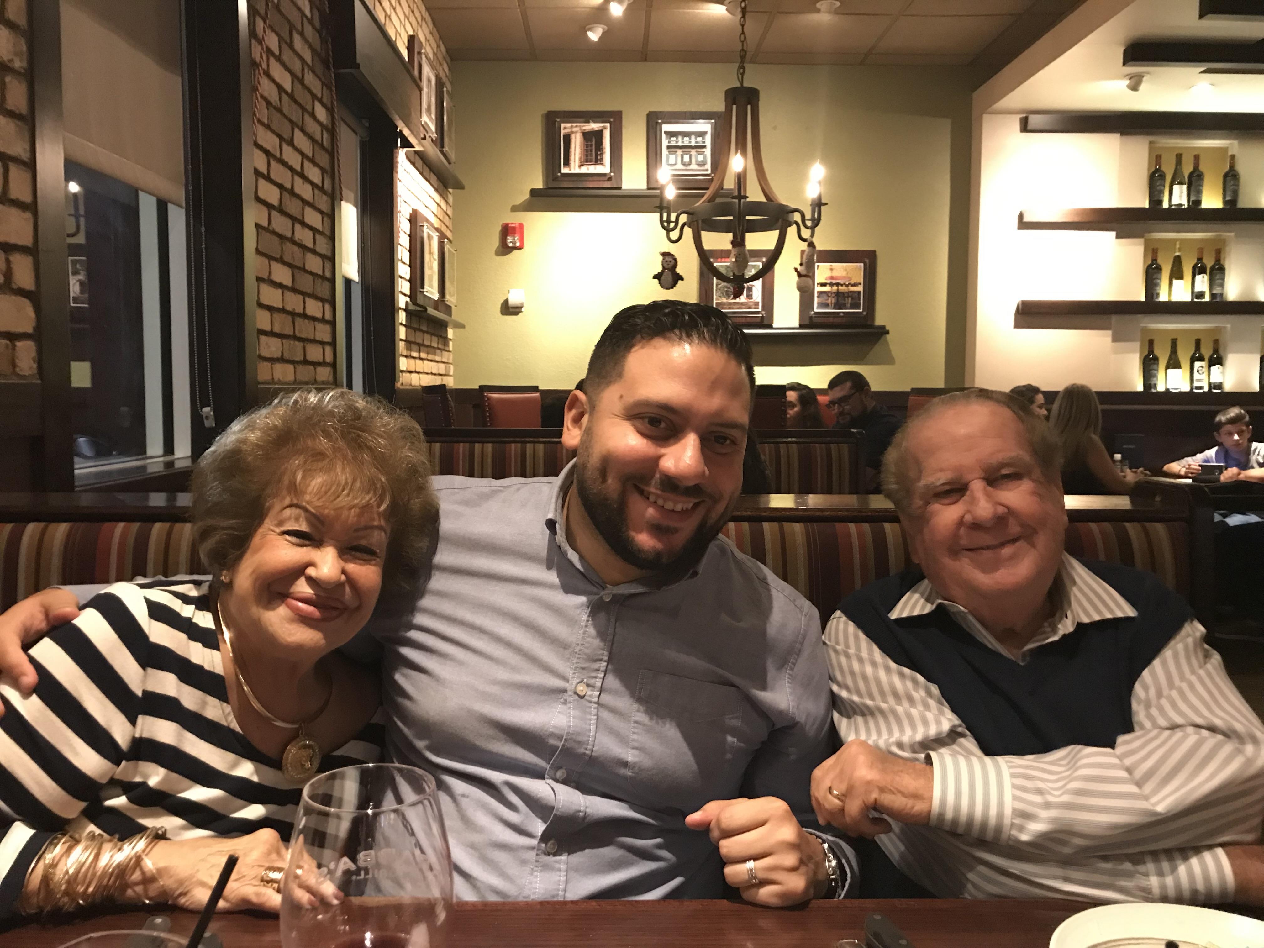 Three people sit at a table in a restaurant smiling and sharing a moment at dinner time.