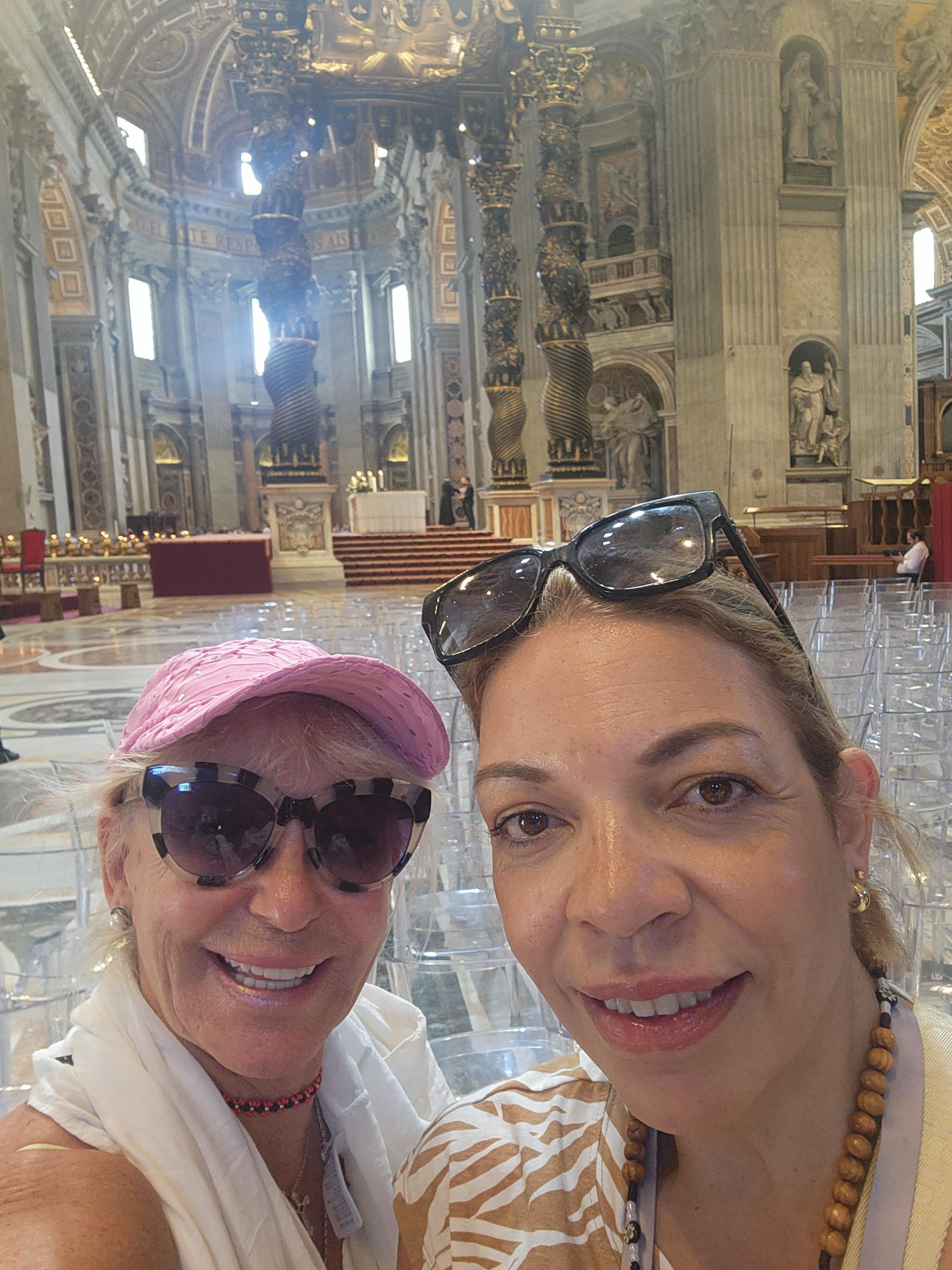 Two women smile and pose for a selfie in a church with tall ceilings and stone walls.