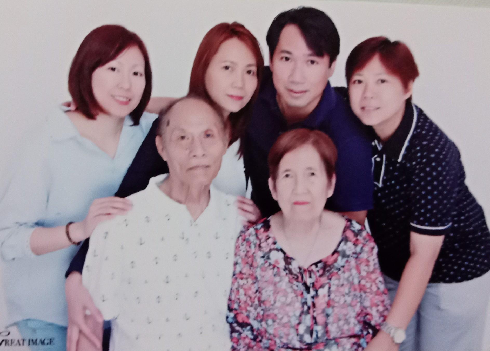Group of six people smiling and standing close together in a room with bright light.