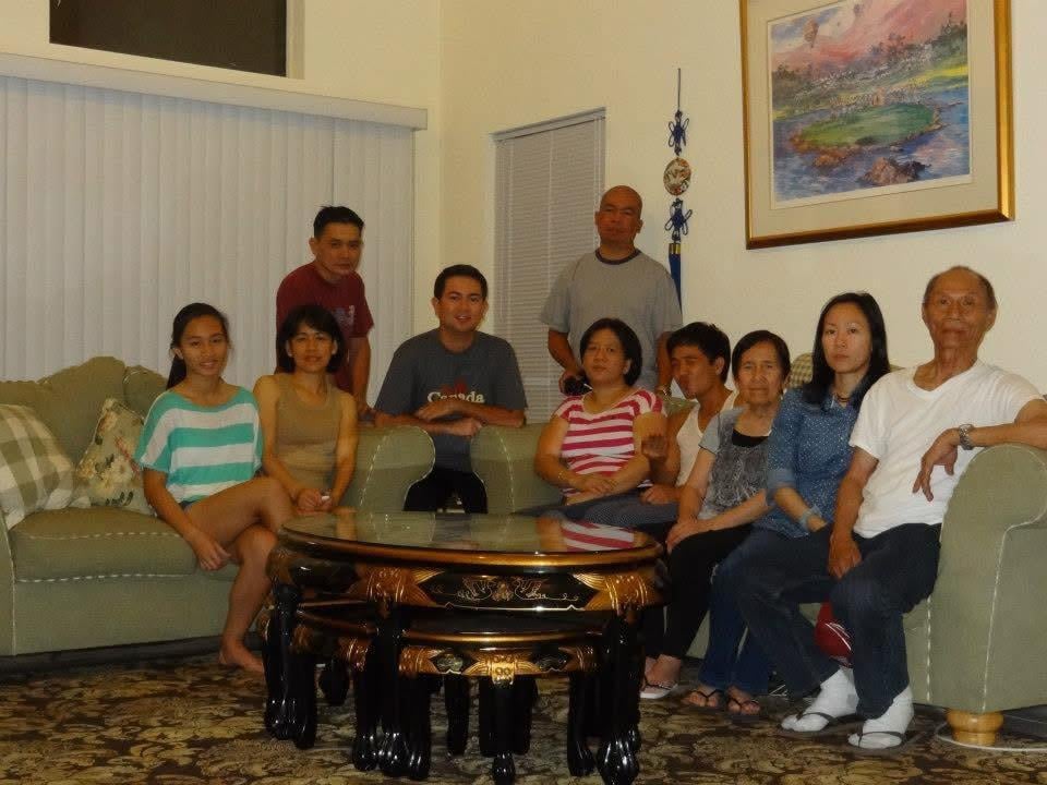 Group of people sit around a table in a living room during a family gathering.