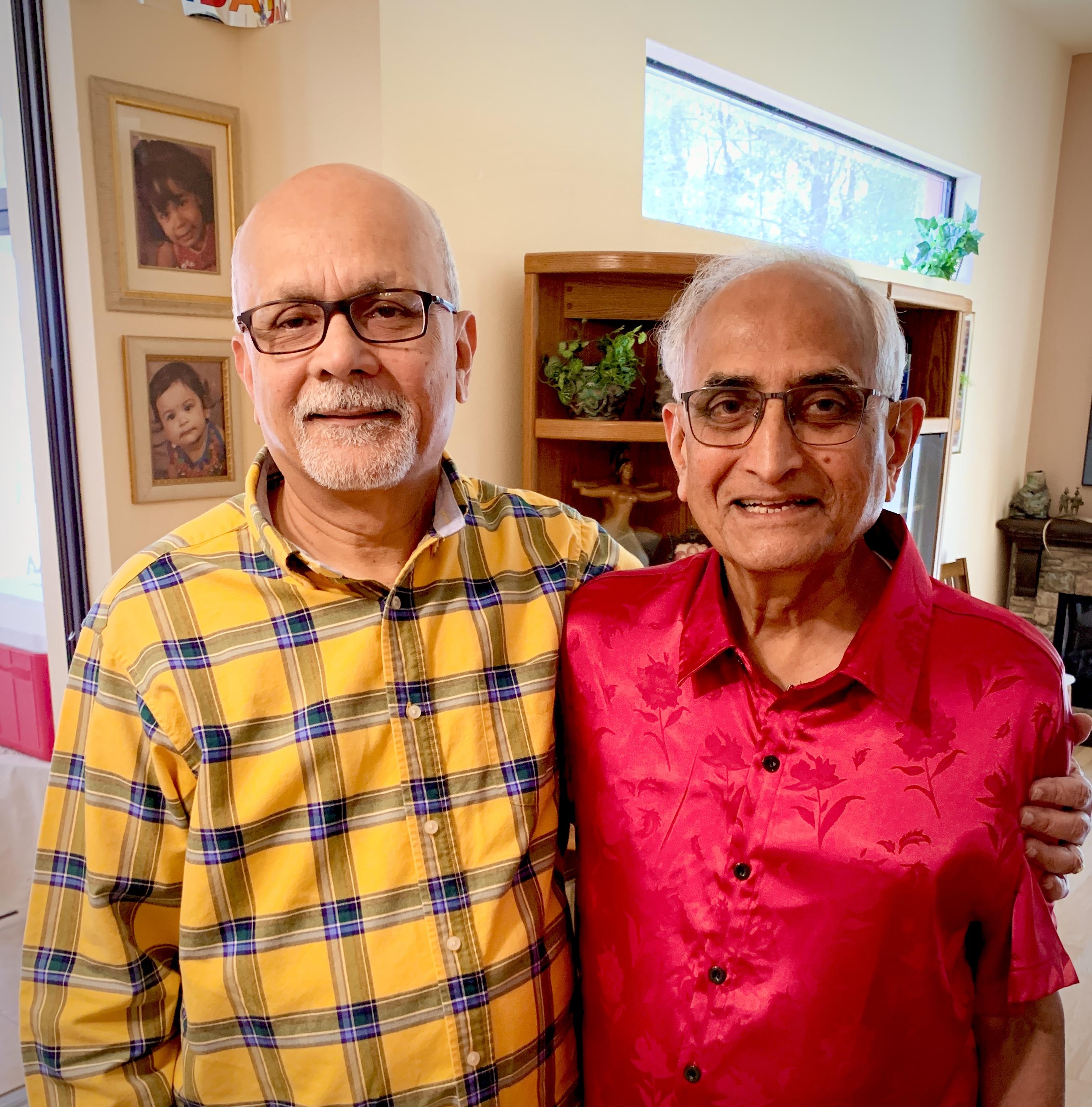 Two men stand together in a well-lit indoor space, both are smiling while facing the camera.