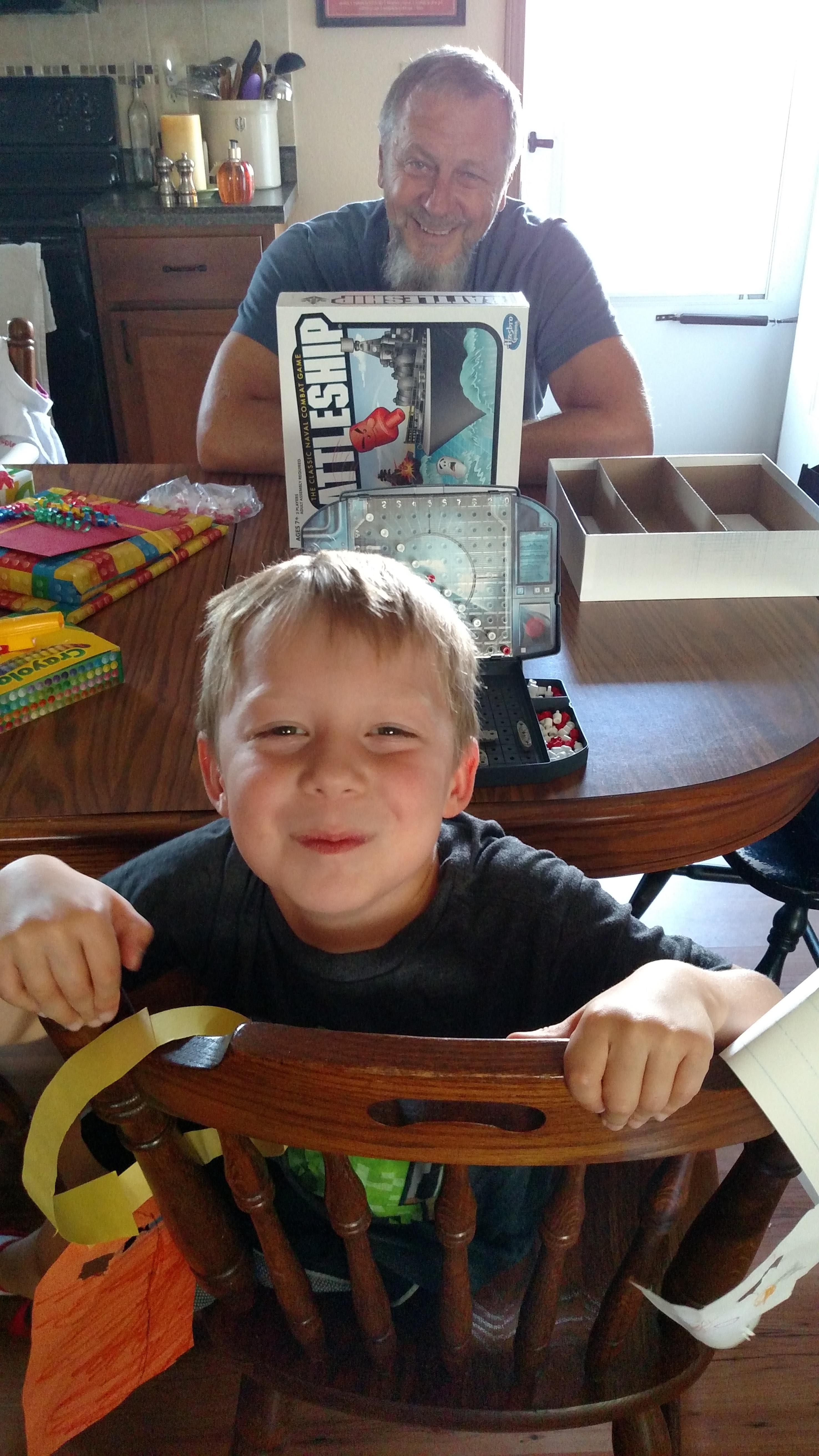 A child enjoys time with family at the table while holding a board game box and smiling happily.