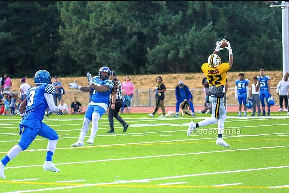 Two teams are playing football on a green field. A player catches the ball while others run.