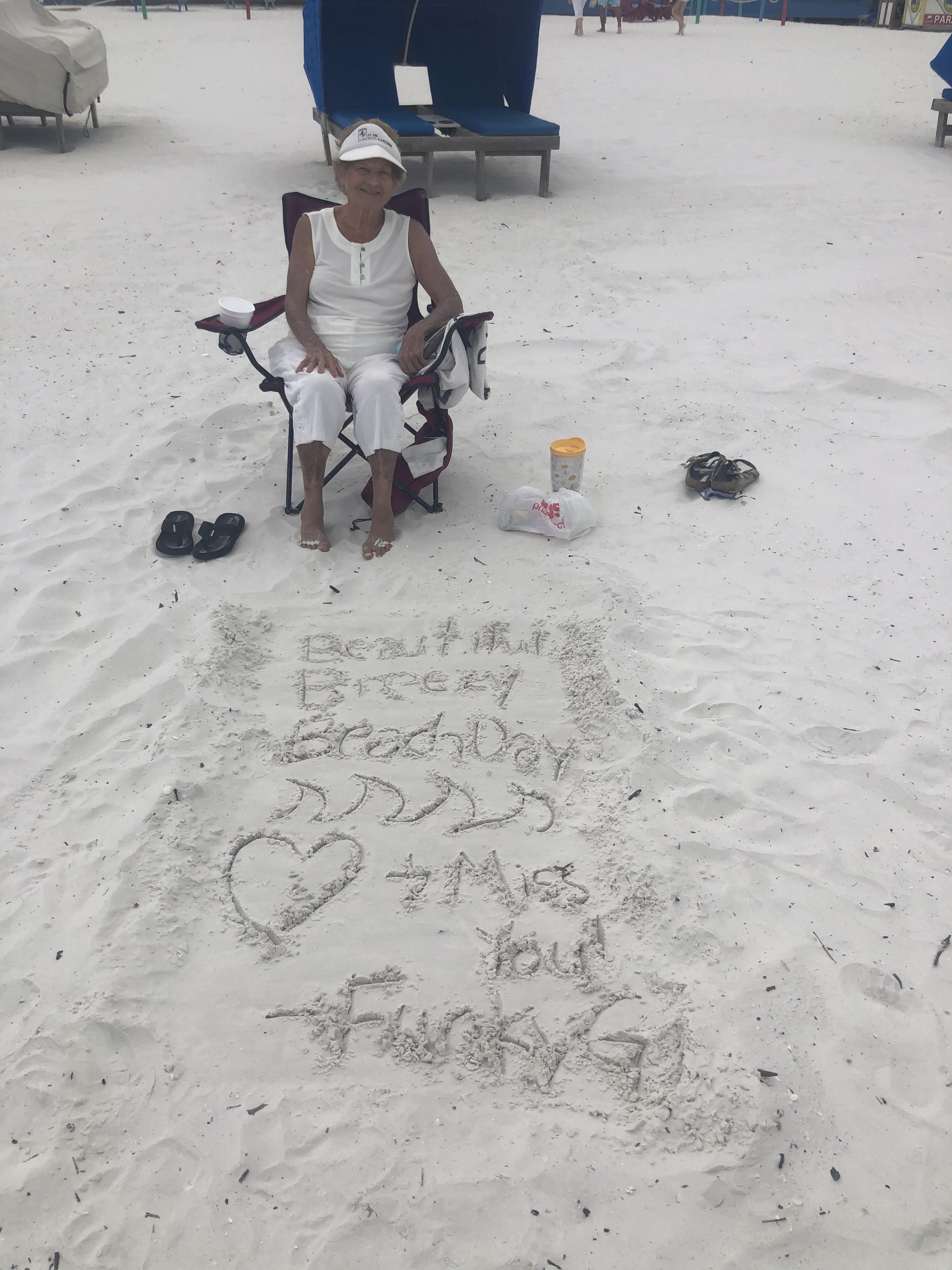 A man sits on a chair at the beach and writes in the sand while enjoying the sun.