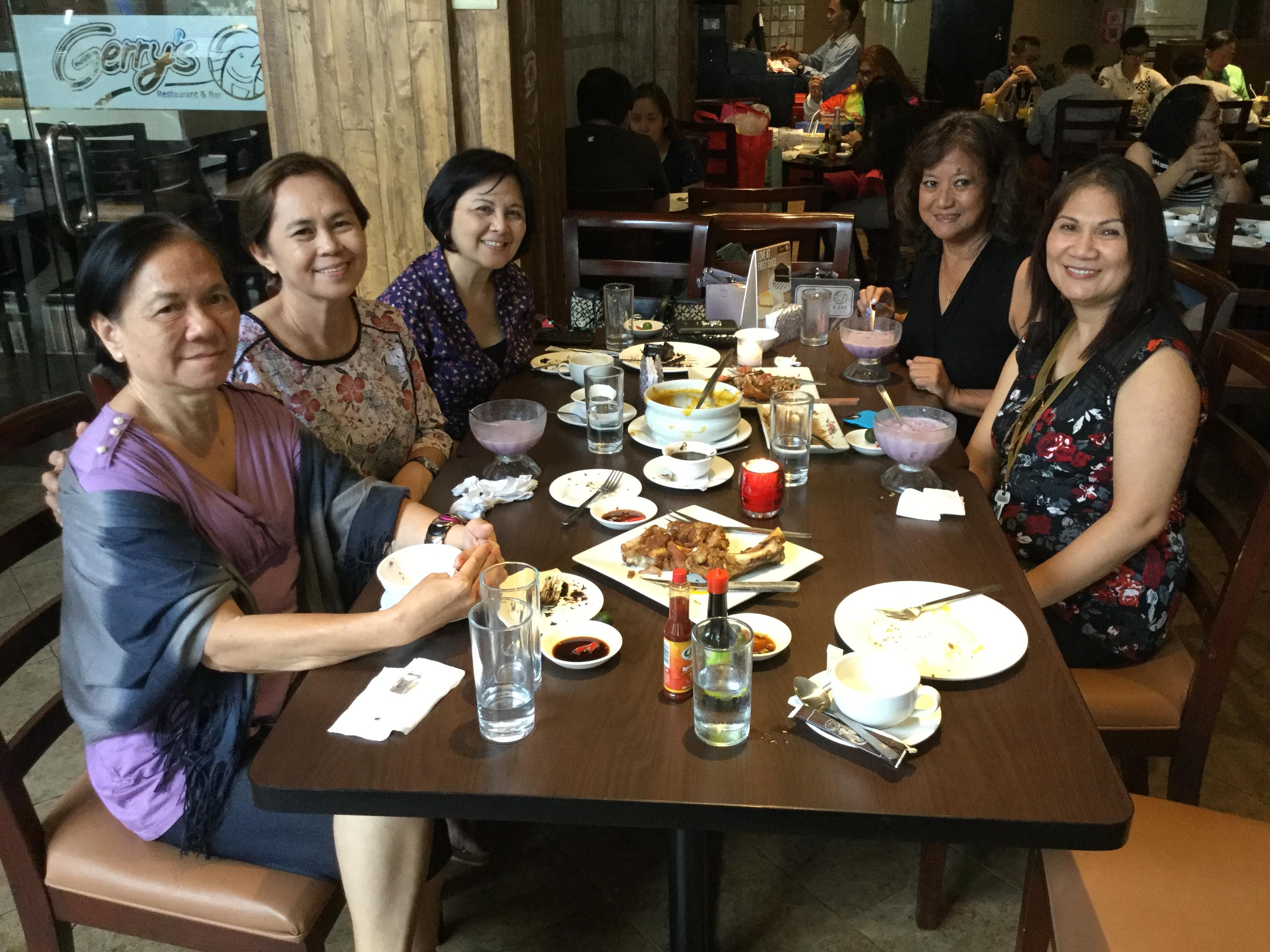 Five friends share laughter and stories over food and drinks at a bustling restaurant.