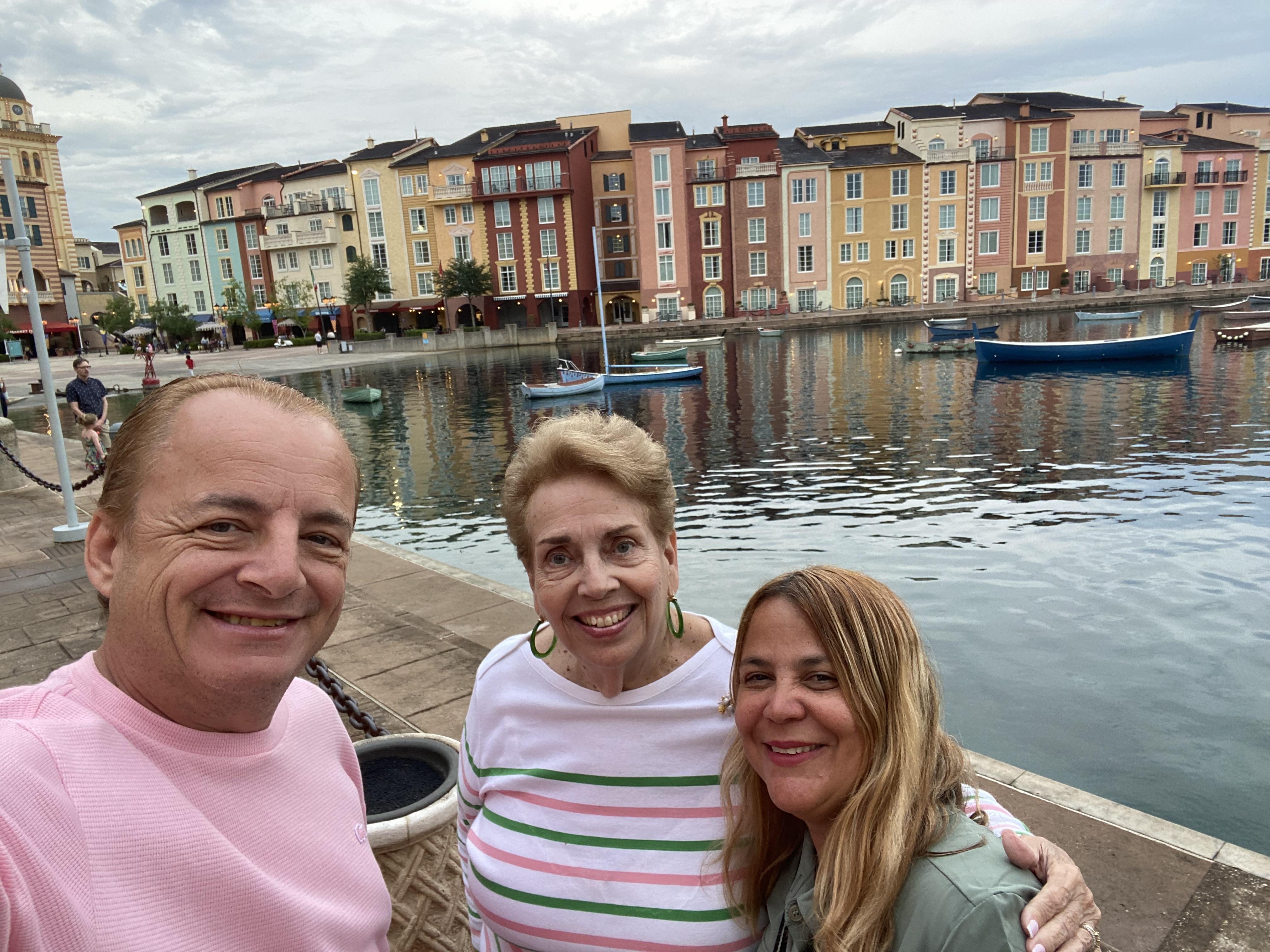 Three friends stand by the waterfront, smiling and enjoying their time together in a vibrant town.