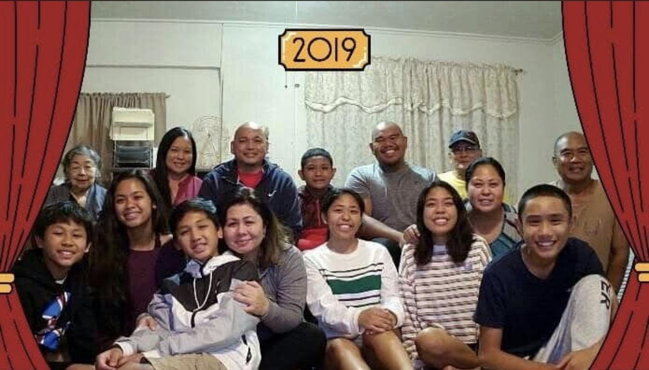 Group of family members gathered together smiling for a picture in a living room setting.