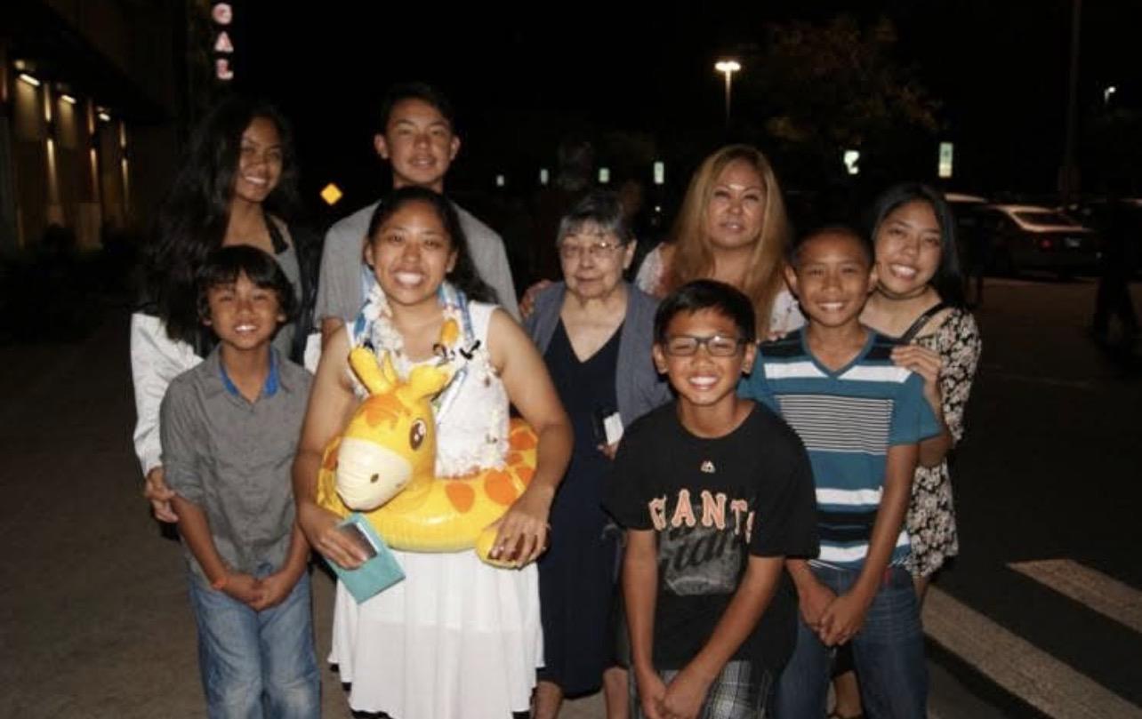 Family members stand together at night, some holding a giraffe toy during a birthday gathering.