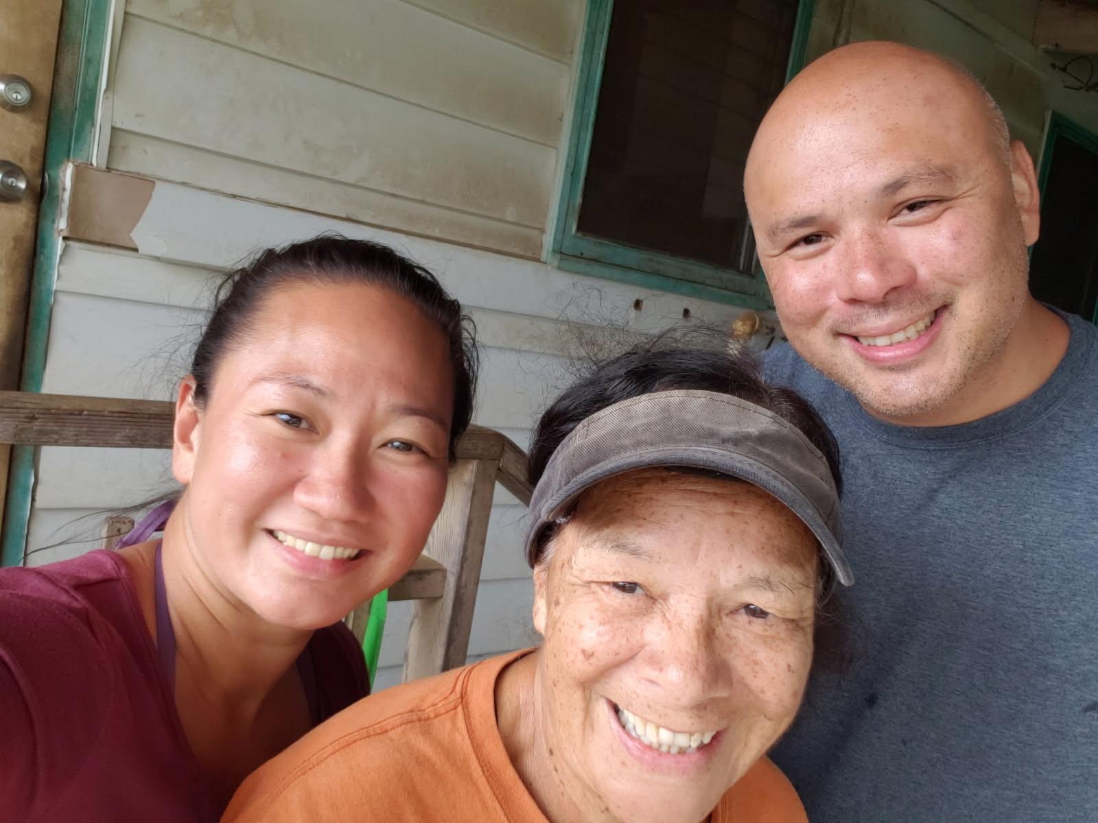 Three people smile together on a porch, enjoying a friendly gathering in a home setting.
