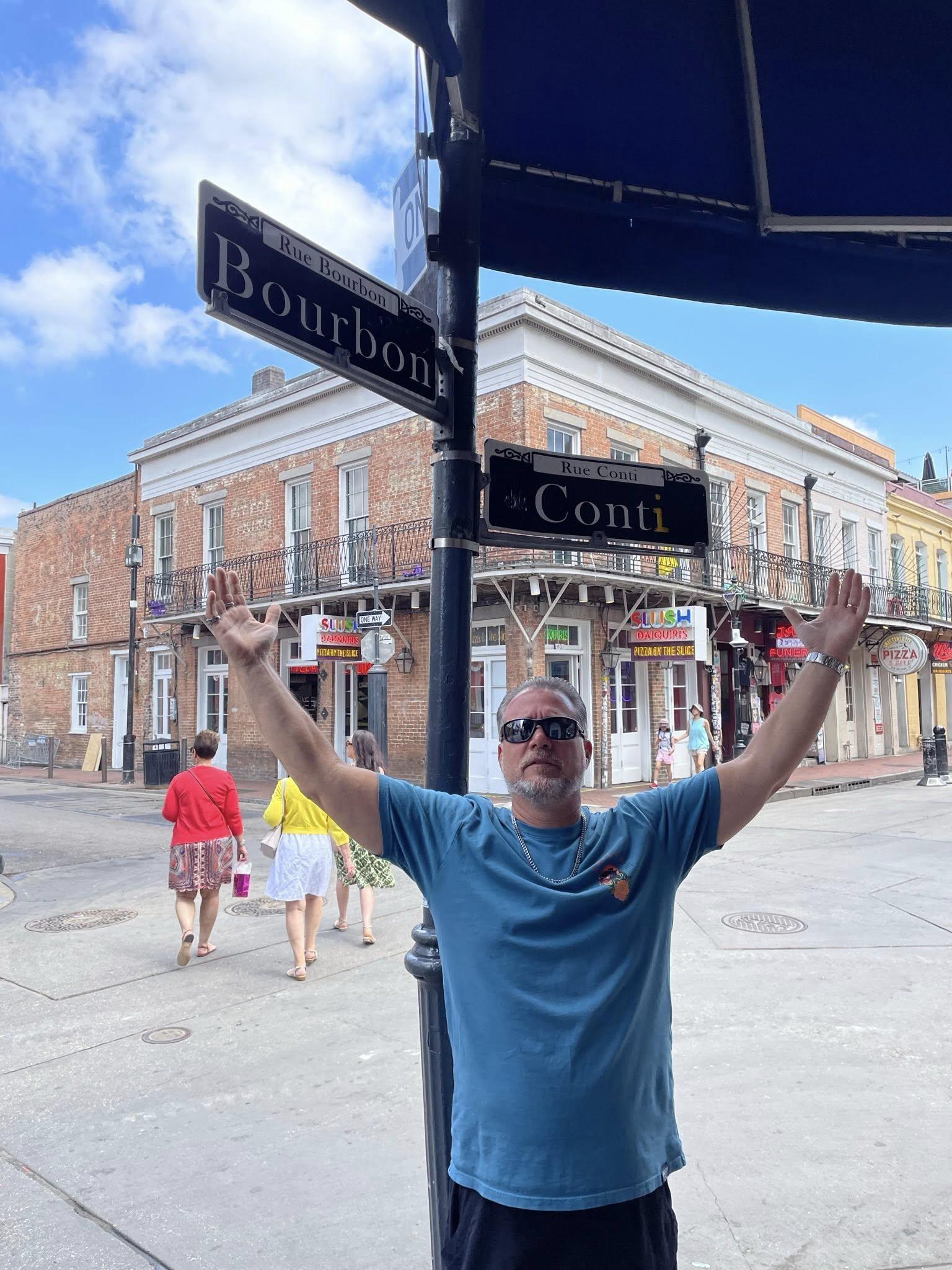 A man stands with arms raised at the intersection of Bourbon Street and Conti Street.