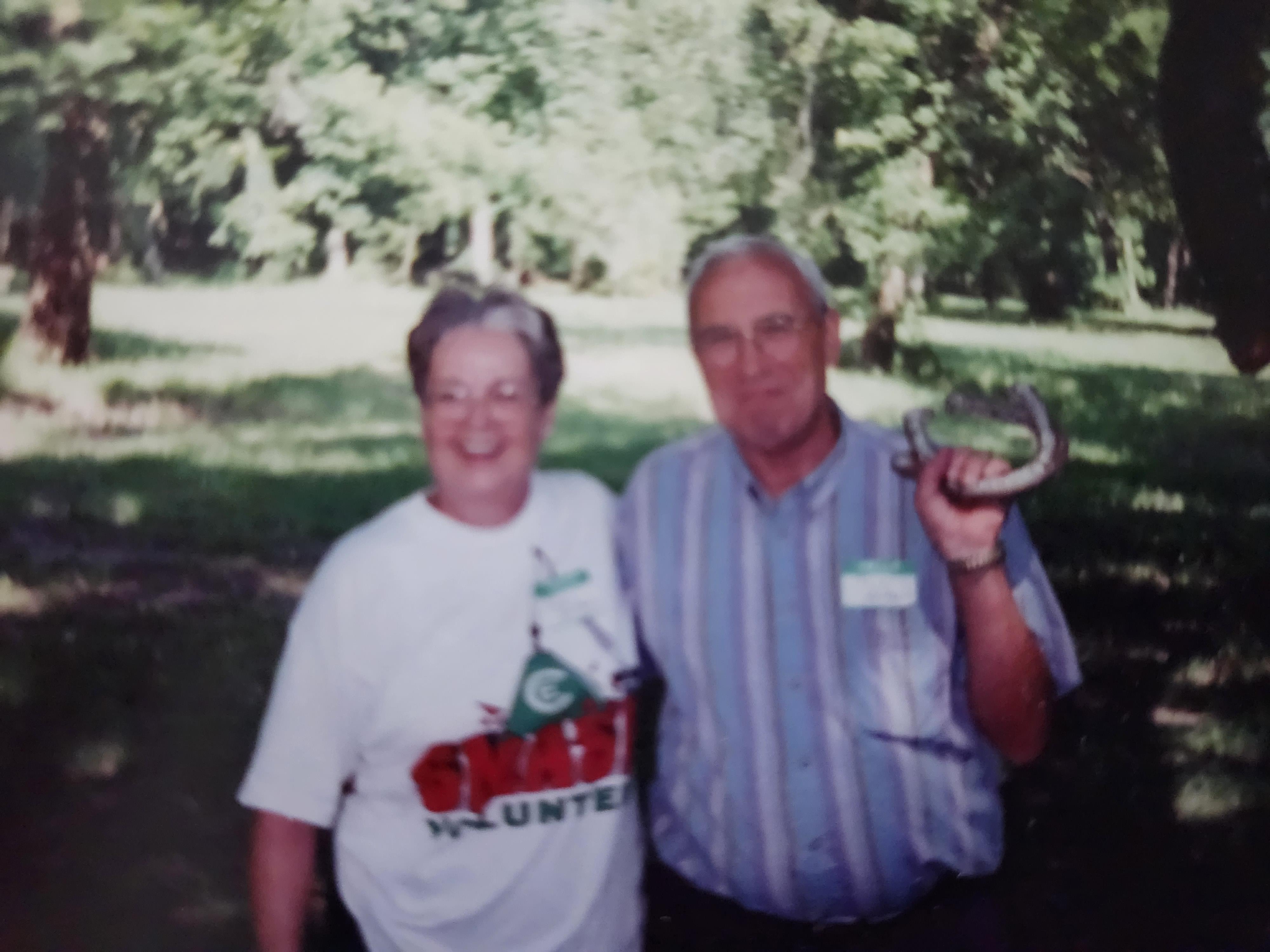 Two people pose together outdoors during a community event with nature in the background.