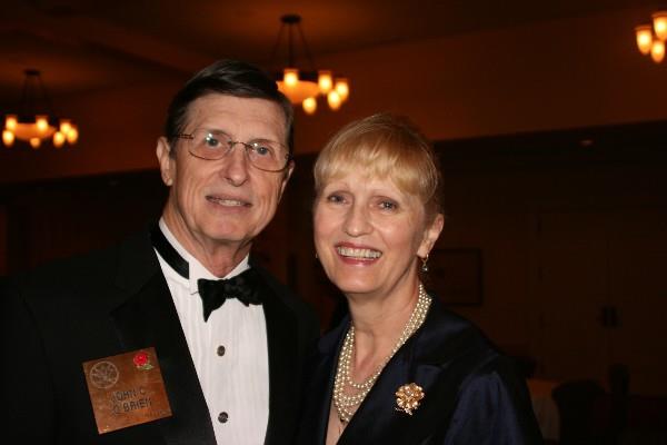 A couple smiles and poses for a picture at a formal gathering in a venue at night.