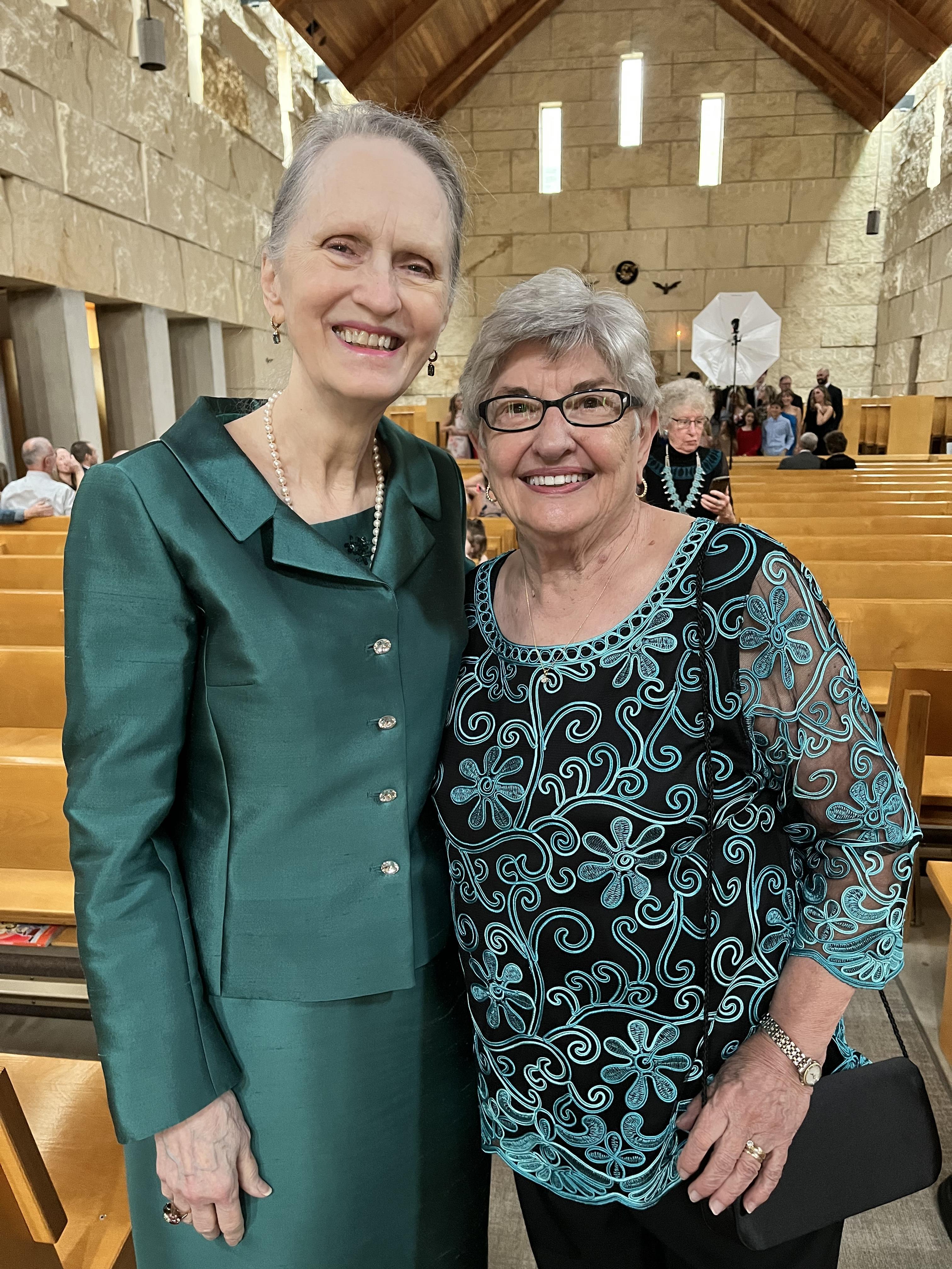 Two women smile together in a church during a lively social gathering.