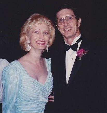 Man and woman stand together at a formal event while smiling and posing for the moment.