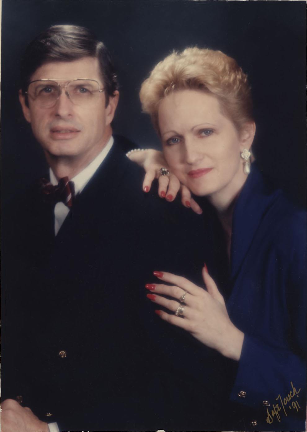 Two people stand together in a studio portrait, showcasing formal attire with smiles.