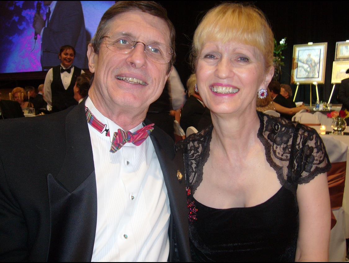 Two people pose together at a formal gathering in the evening, smiling for the camera.