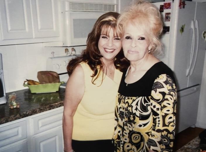 Two women stand close in a kitchen. They have joyful expressions as they pose together.