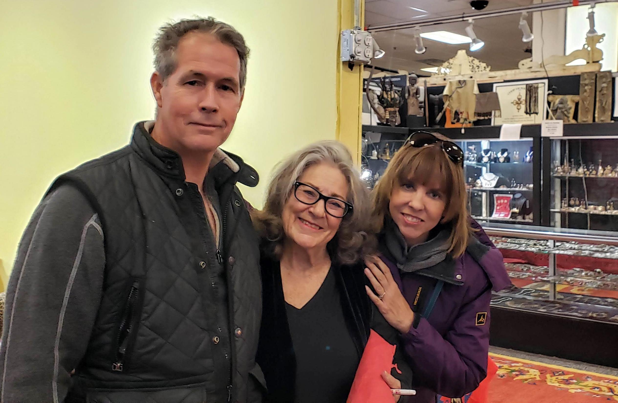 Three people pose and smile in a store. They seem to enjoy each other's company and have fun.