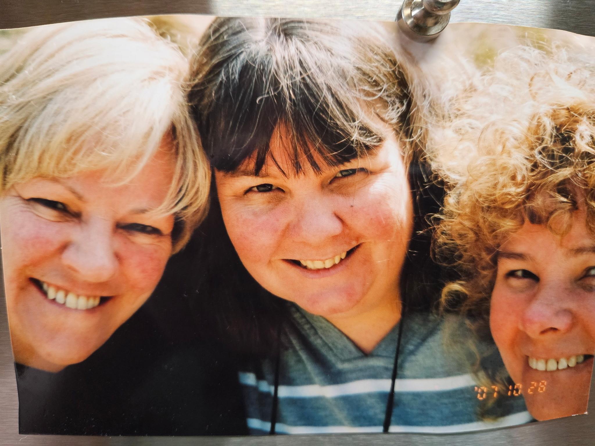 Three friends are enjoying a moment together while smiling and posing for a casual photo outdoors.