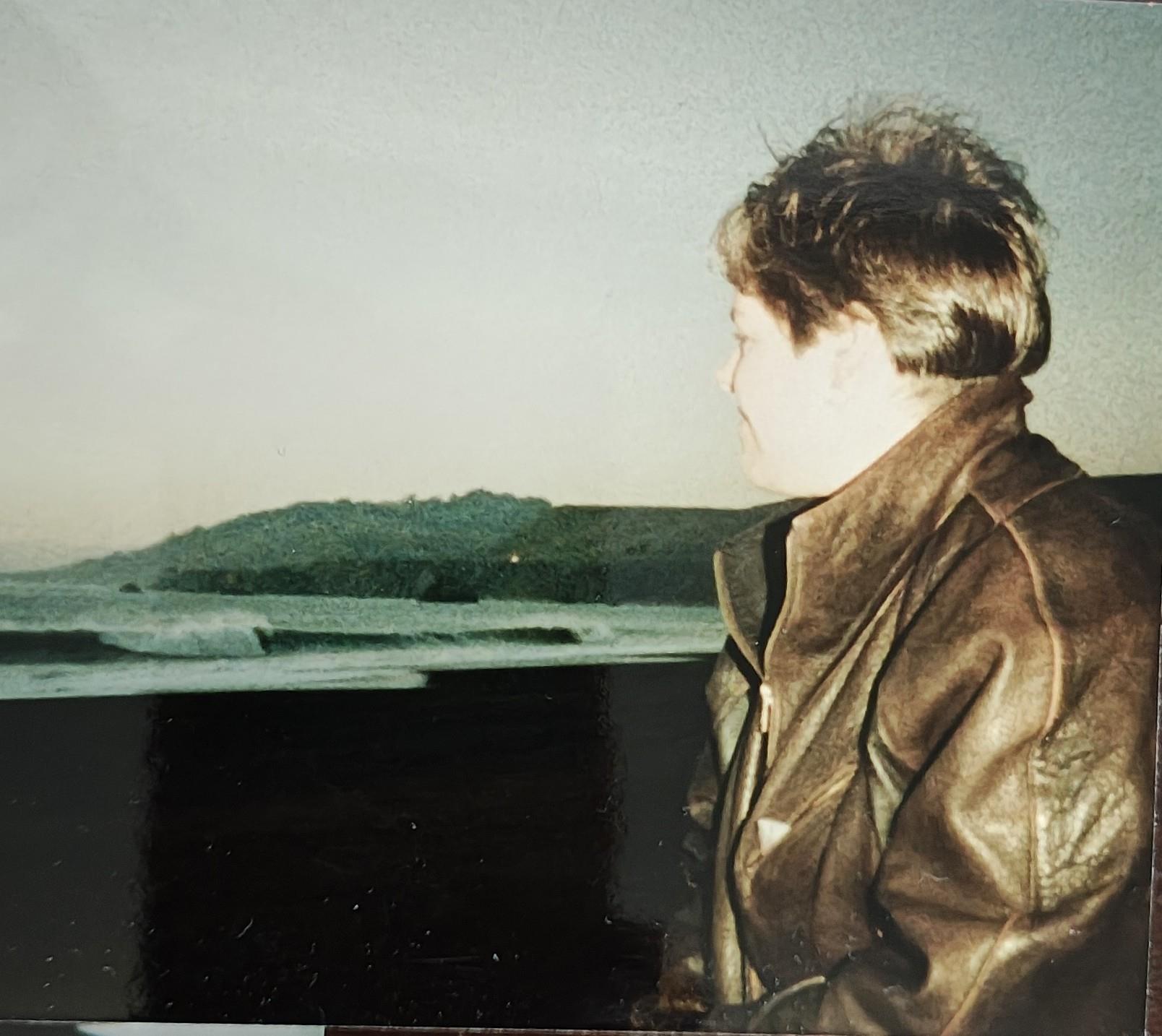 A person looks out at the waves from a shore in the evening light near a quiet area.