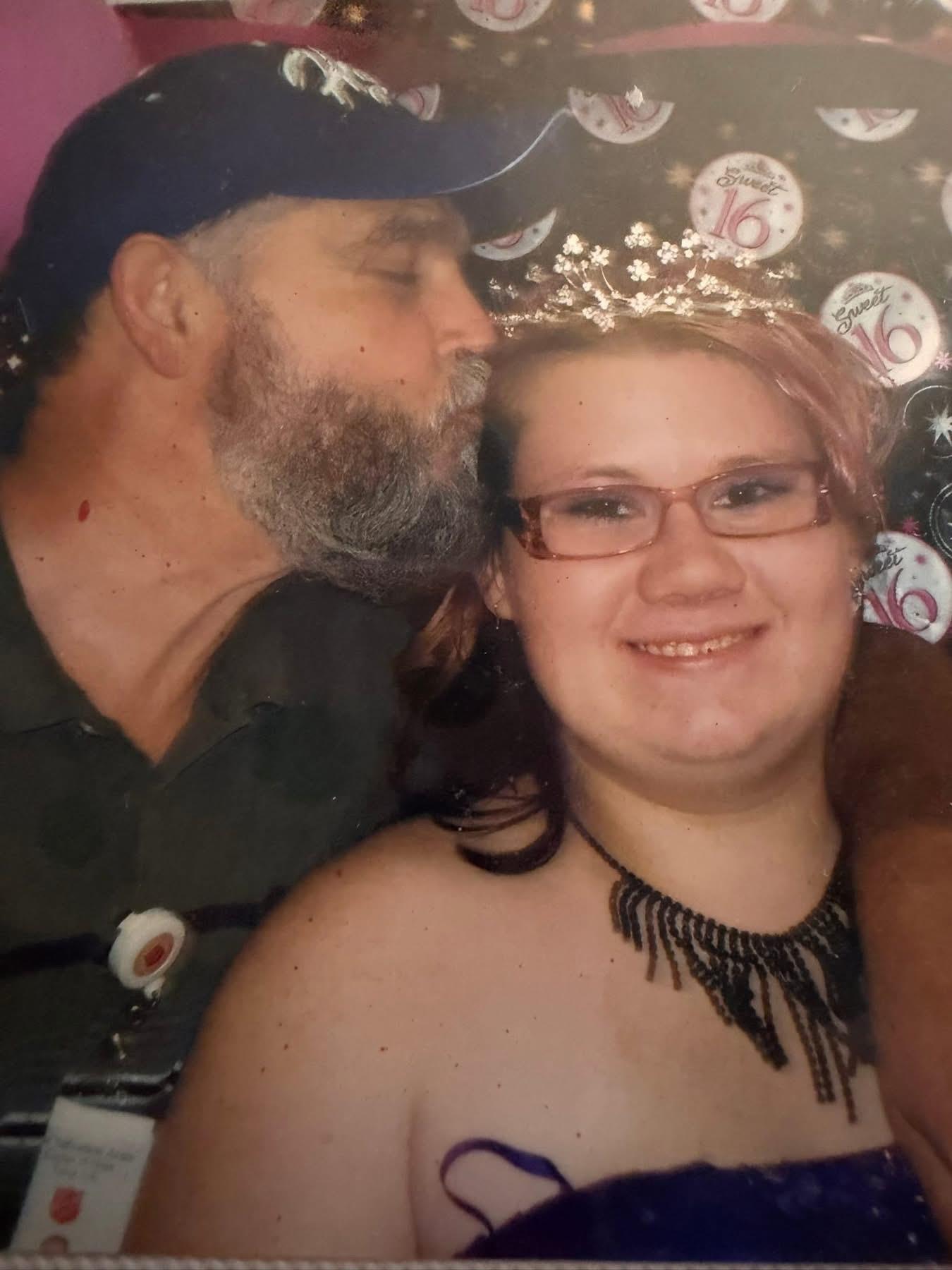 A father shows affection to his daughter at a gathering in their home during the evening.
