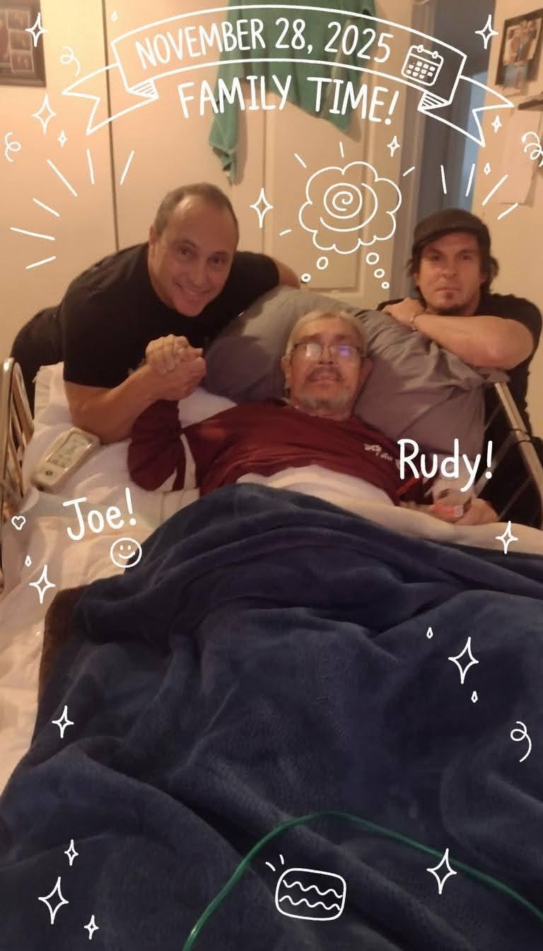 Two men stand near their friend in bed, holding hands and sharing a moment together.