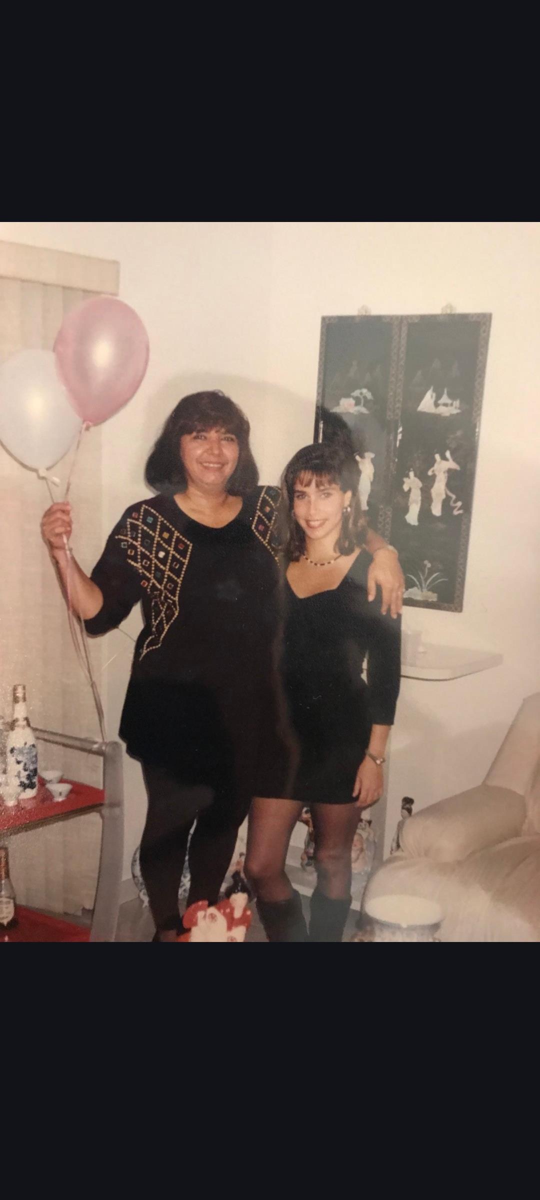 Two women smile and hold balloons together at a party, enjoying the moment.