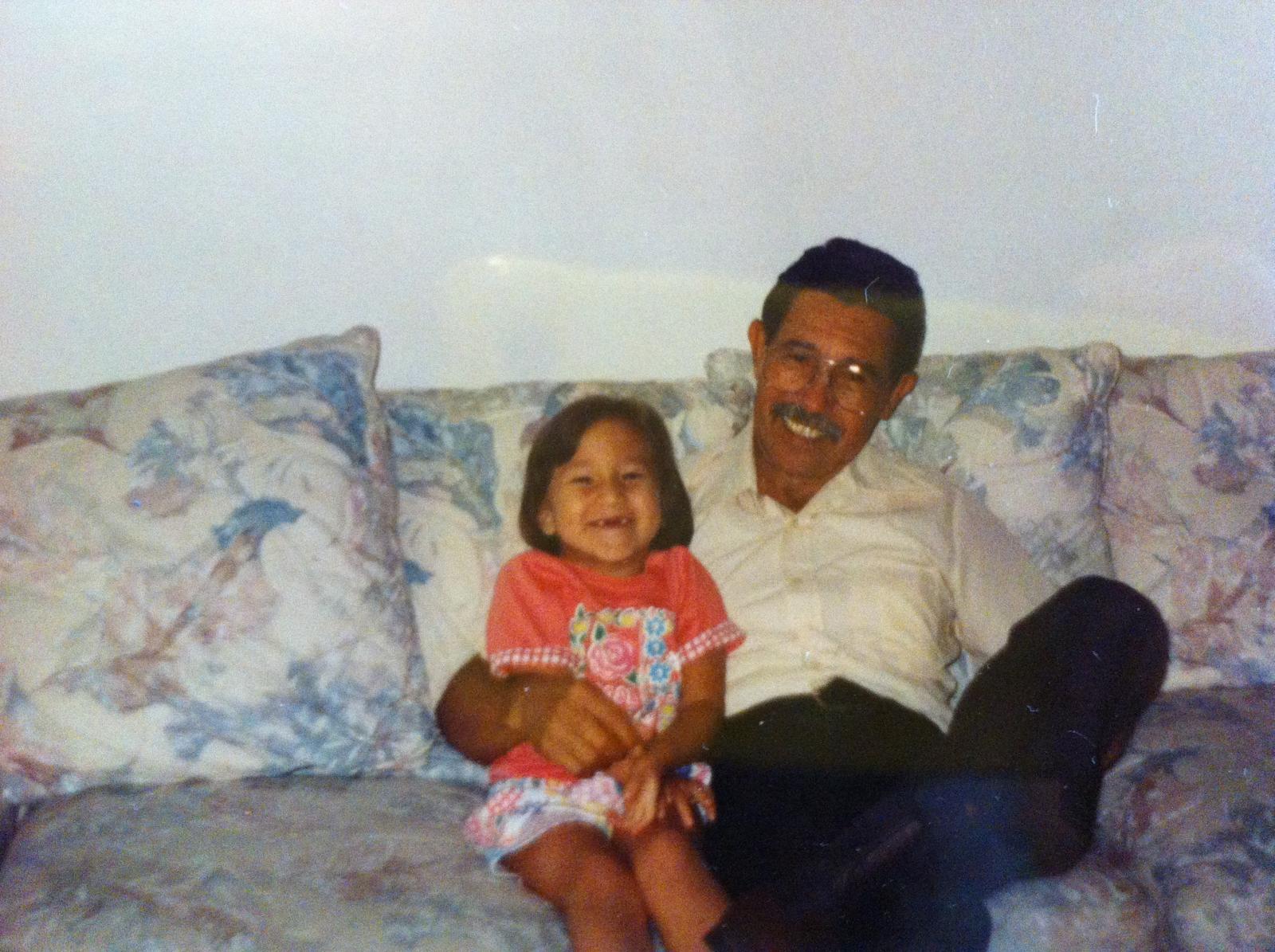 A man sits on a couch holding a girl who is smiling and laughing. They are inside a home.