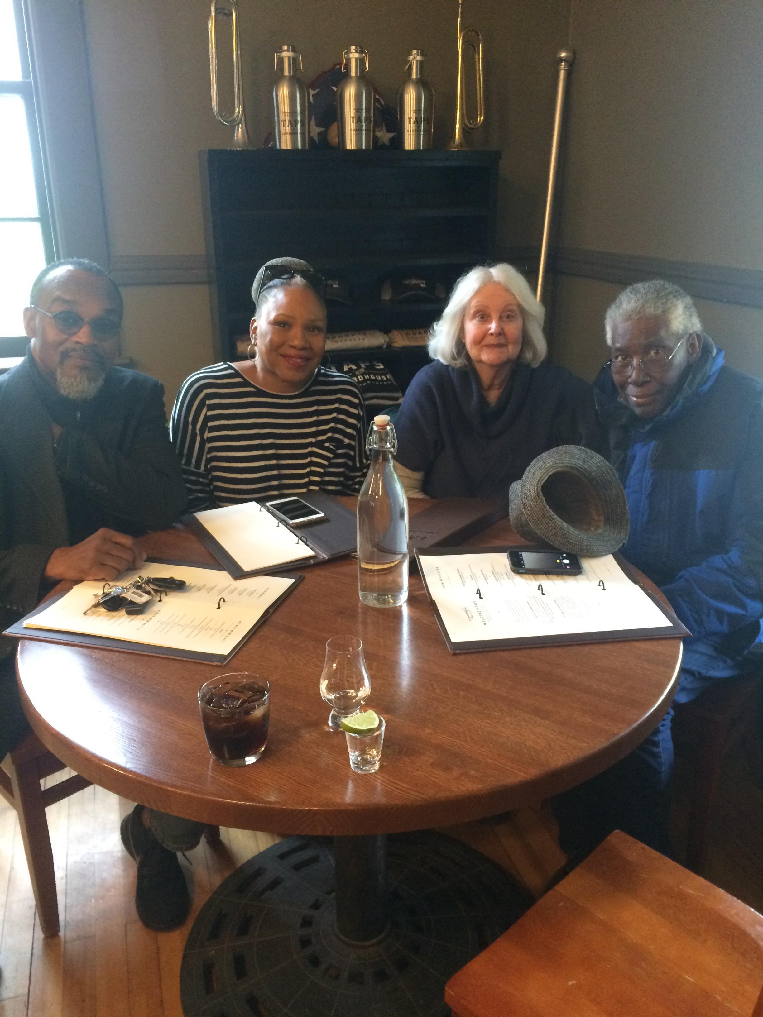 Four friends sit together at a round table in a restaurant sharing drinks and looking at menus.