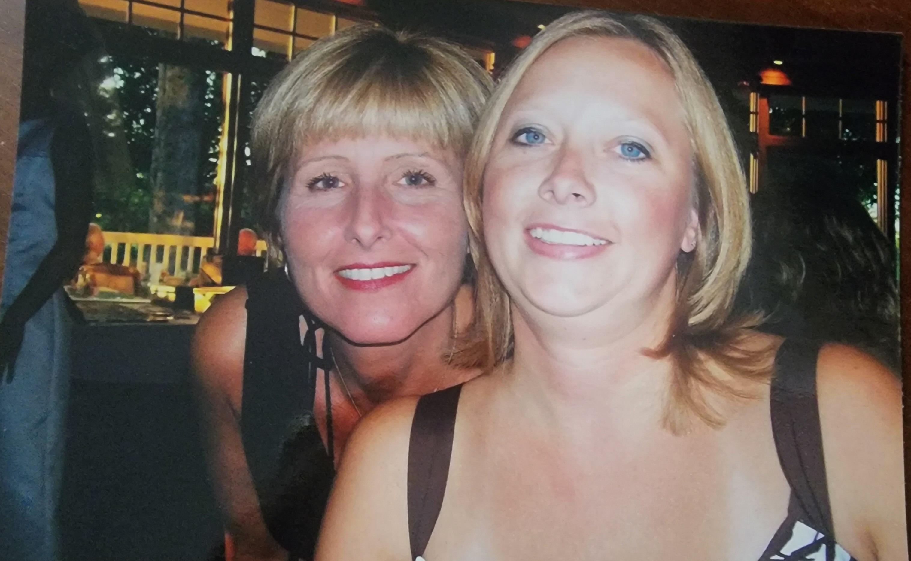 Two women are laughing and taking a fun picture together at a gathering in the evening.