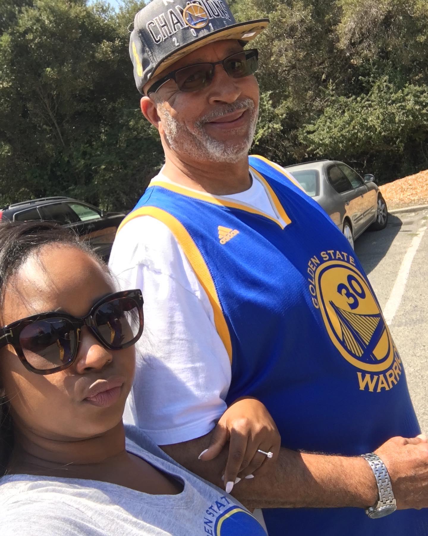 A man and woman walk hand in hand in a park on a sunny day. They look happy and relaxed.