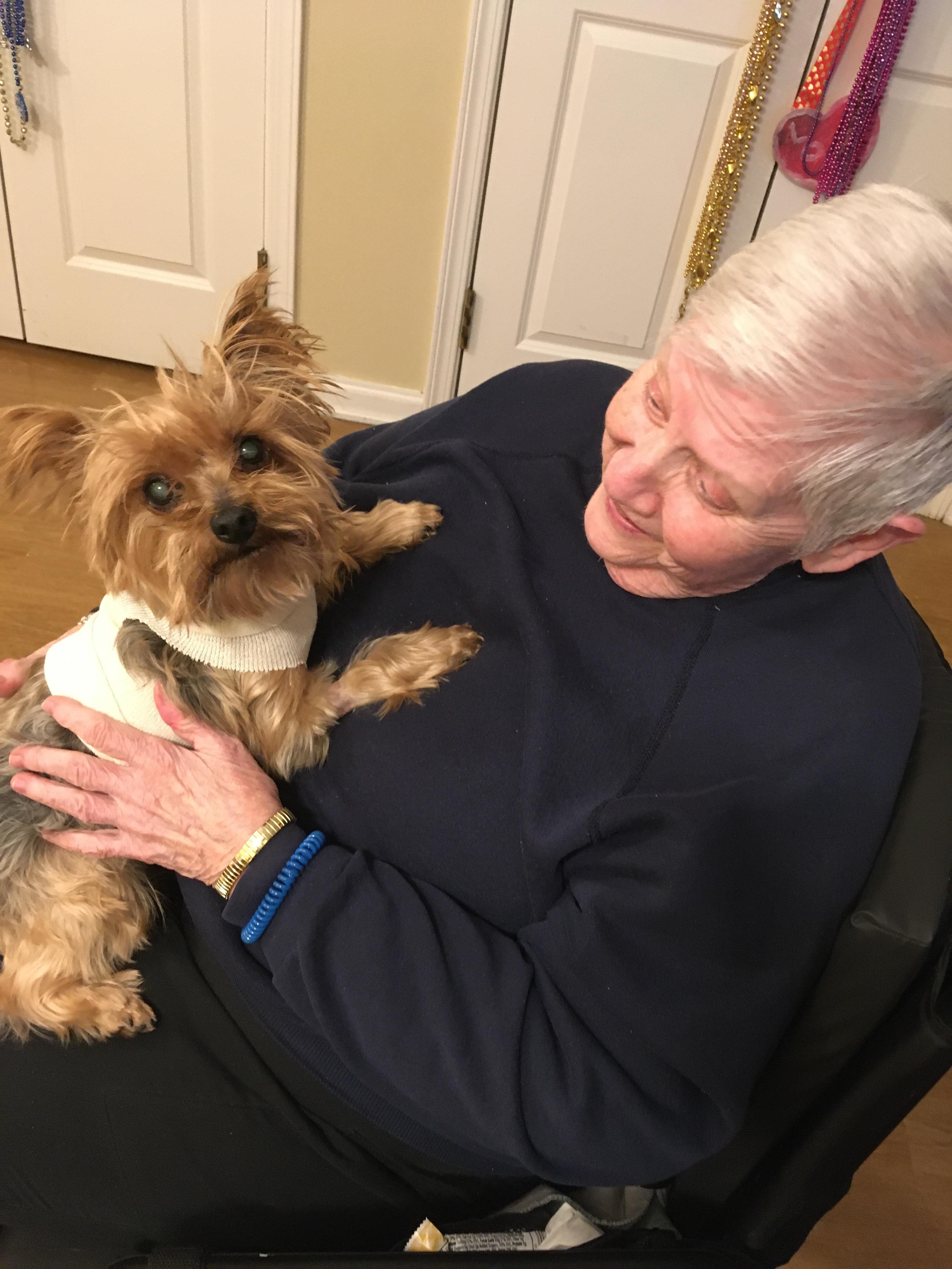 Senior person sits and holds a small dog close while sharing a moment together indoors.