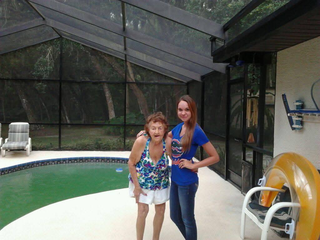 Two individuals stand near a swimming pool in a patio area surrounded by screens.